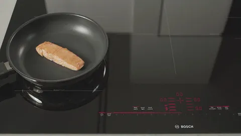 Frying pan on Bosch Induction cooktop, cooking a piece of food.