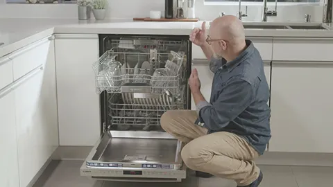 Man inspecting open Bosch dishwasher in kitchen, checking appliance functionality.