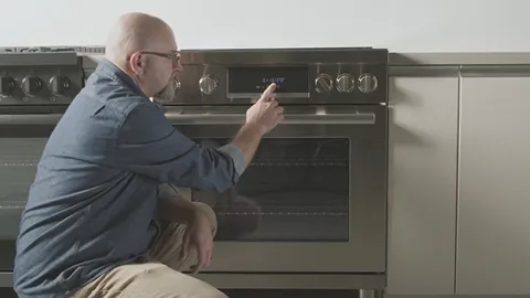 Man in casual clothes examining Bosch oven controls in kitchen.