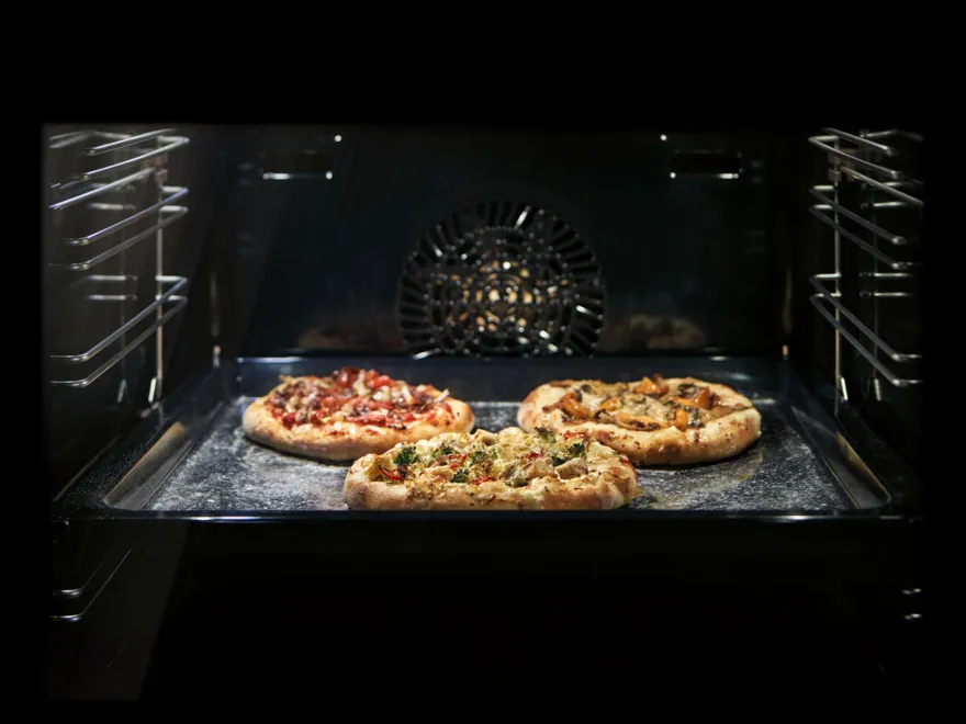 Freshly baked pizzas and pastries in a dark oven, creating a warm, inviting atmosphere.