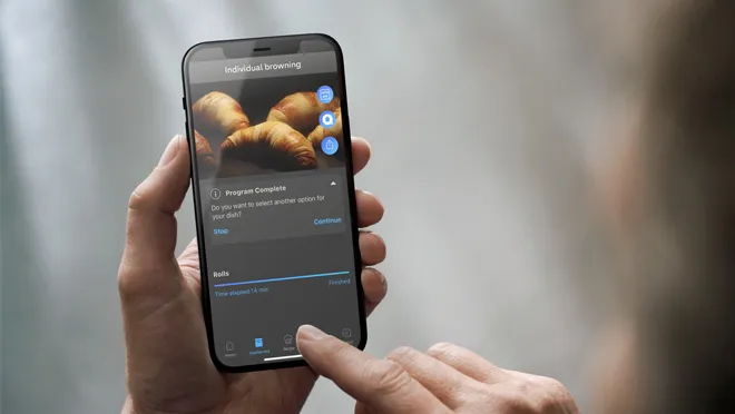 Smartphone displaying image of croissants, hands holding device, blurred background.