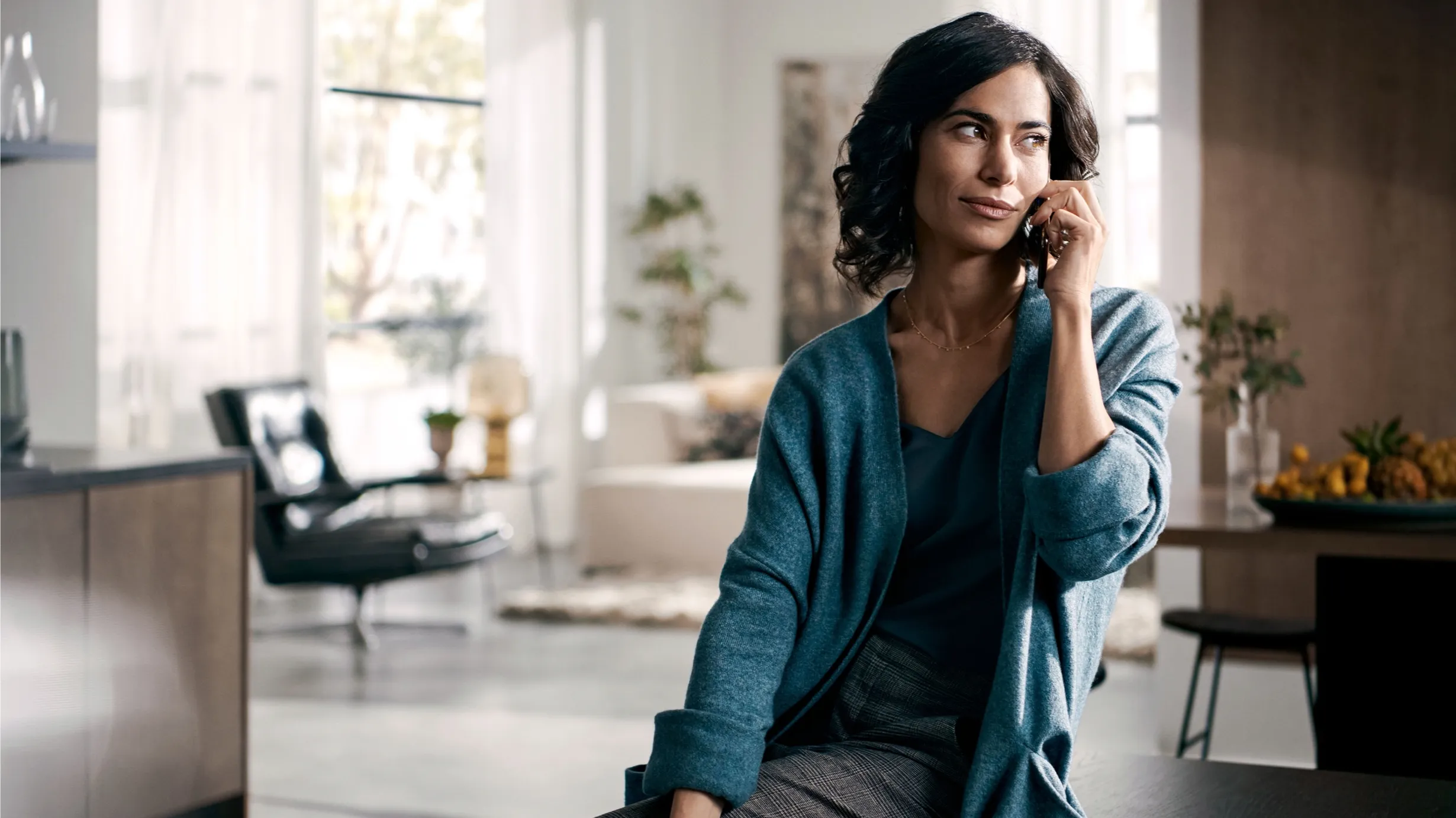 Frau in teal cardigan sitzen in gemütlichen Haus innen, lächelnd und aussehend nachdenklich.