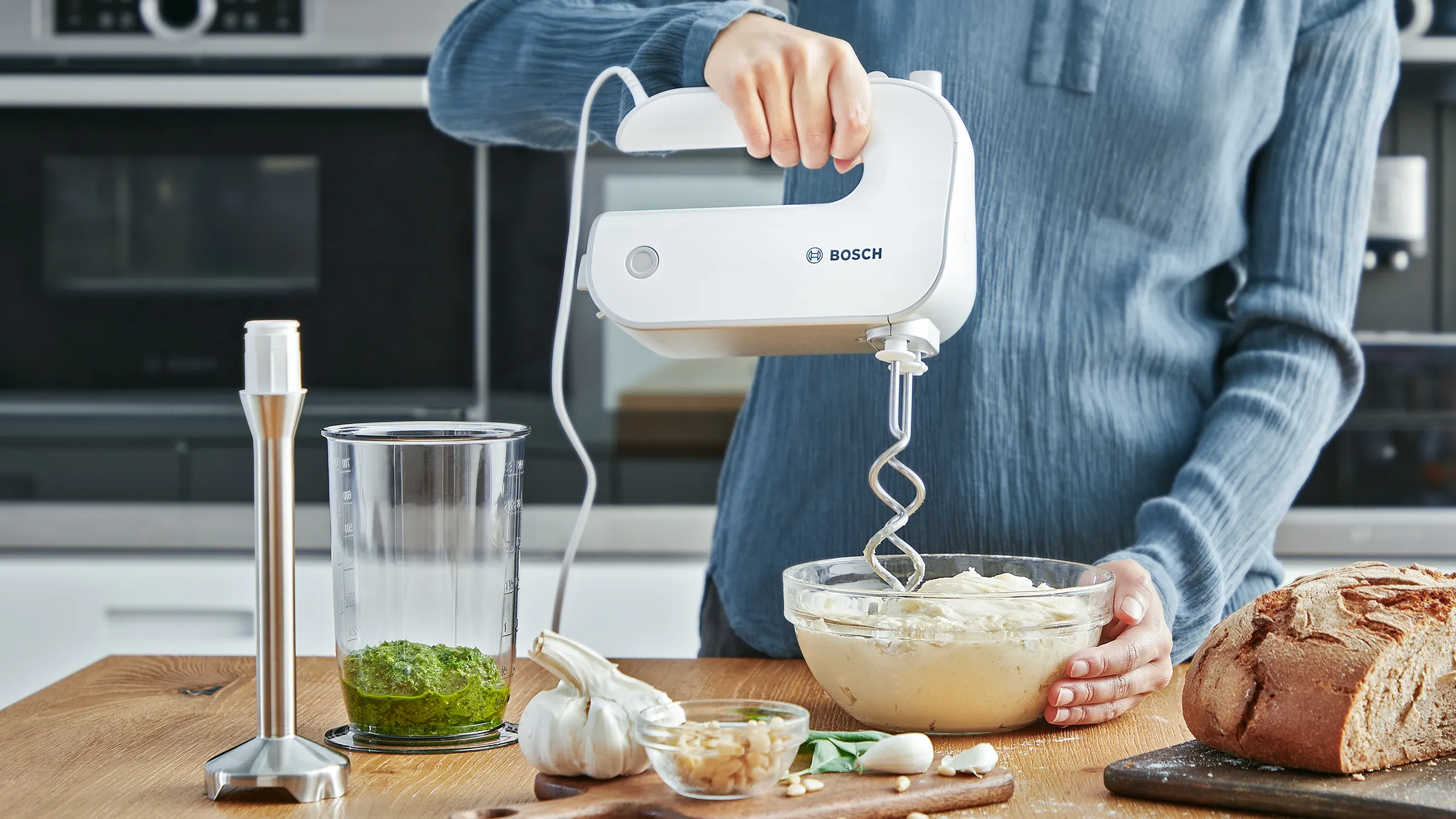 A person kneading dough with an ErgoMixx hand mixer, next to a blending shaft.