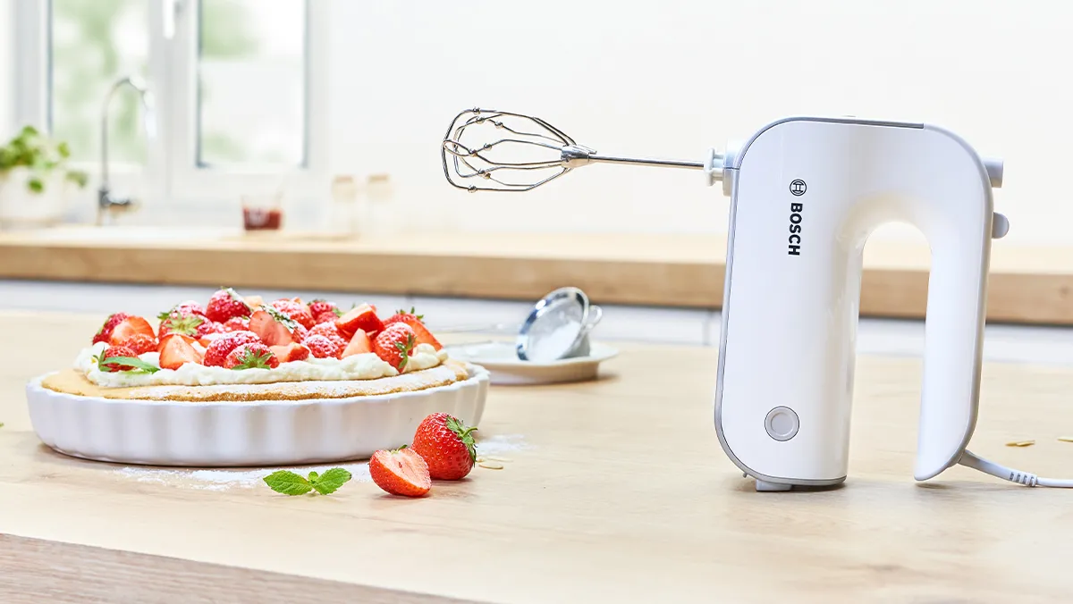 Styline hand mixer with beaters on kitchen worktop next to whipped cream and raspberry cake.