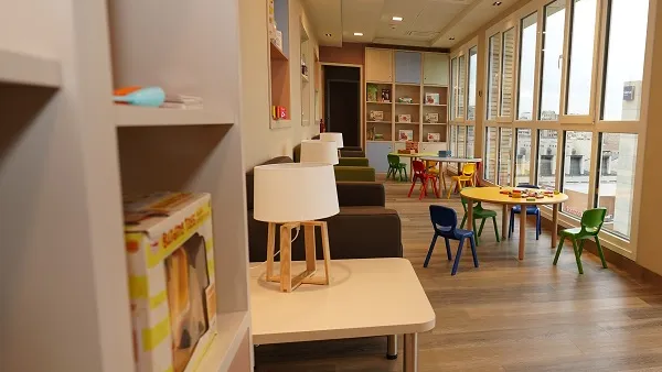Aula luminosa y moderna con muebles coloridos, estanterías y grandes ventanales. 