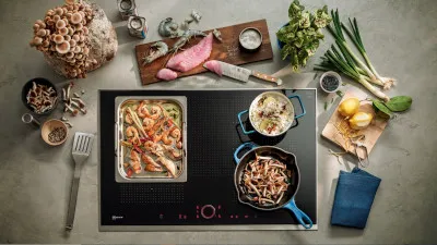 Une vue de dessus d'une cuisine remplie d'ingrédients frais, de casseroles sur une plaque à induction et d'ustensiles, montrant la préparation culinaire.