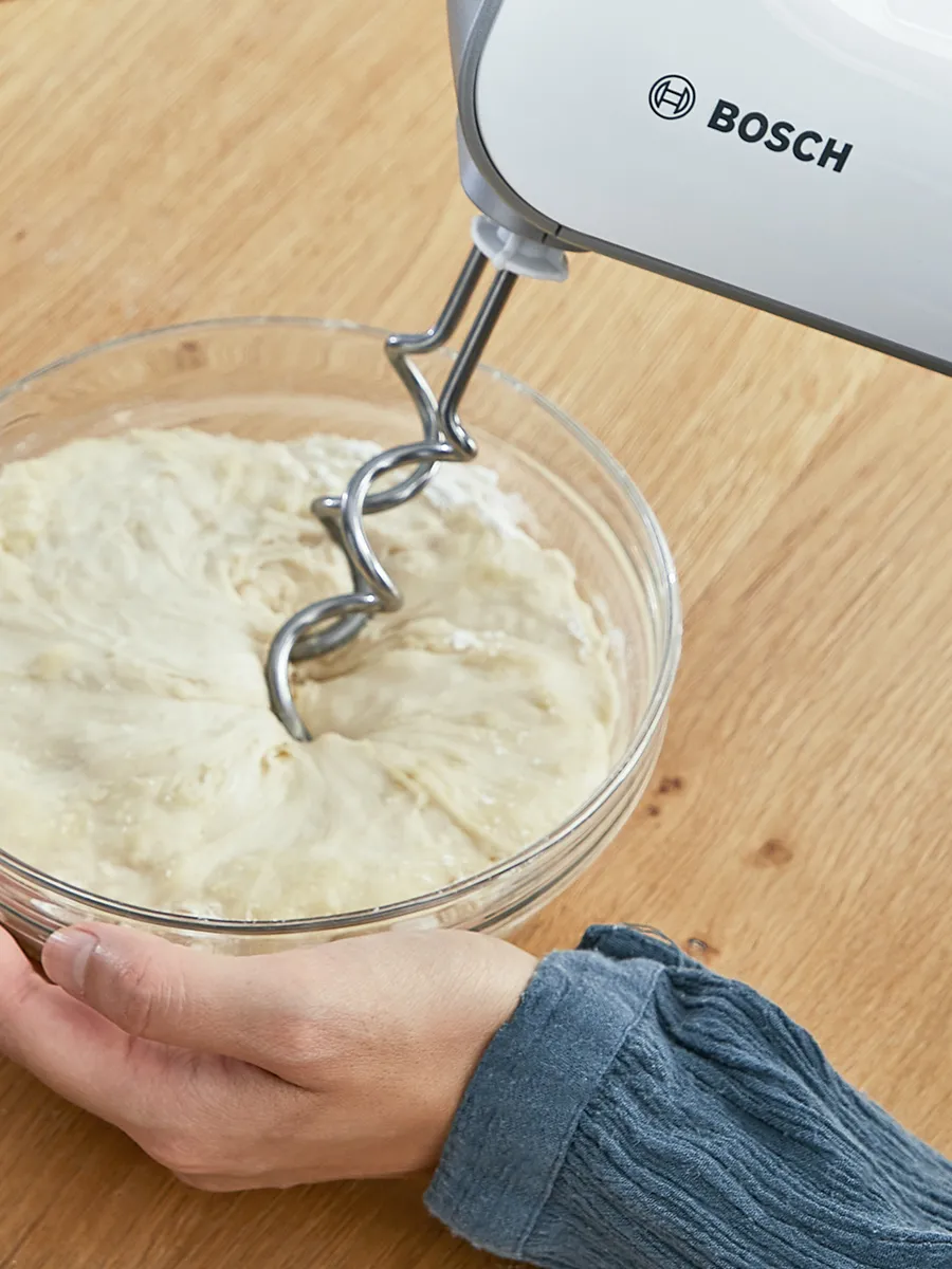 A person kneading a dough with the Bosch hand mixer.