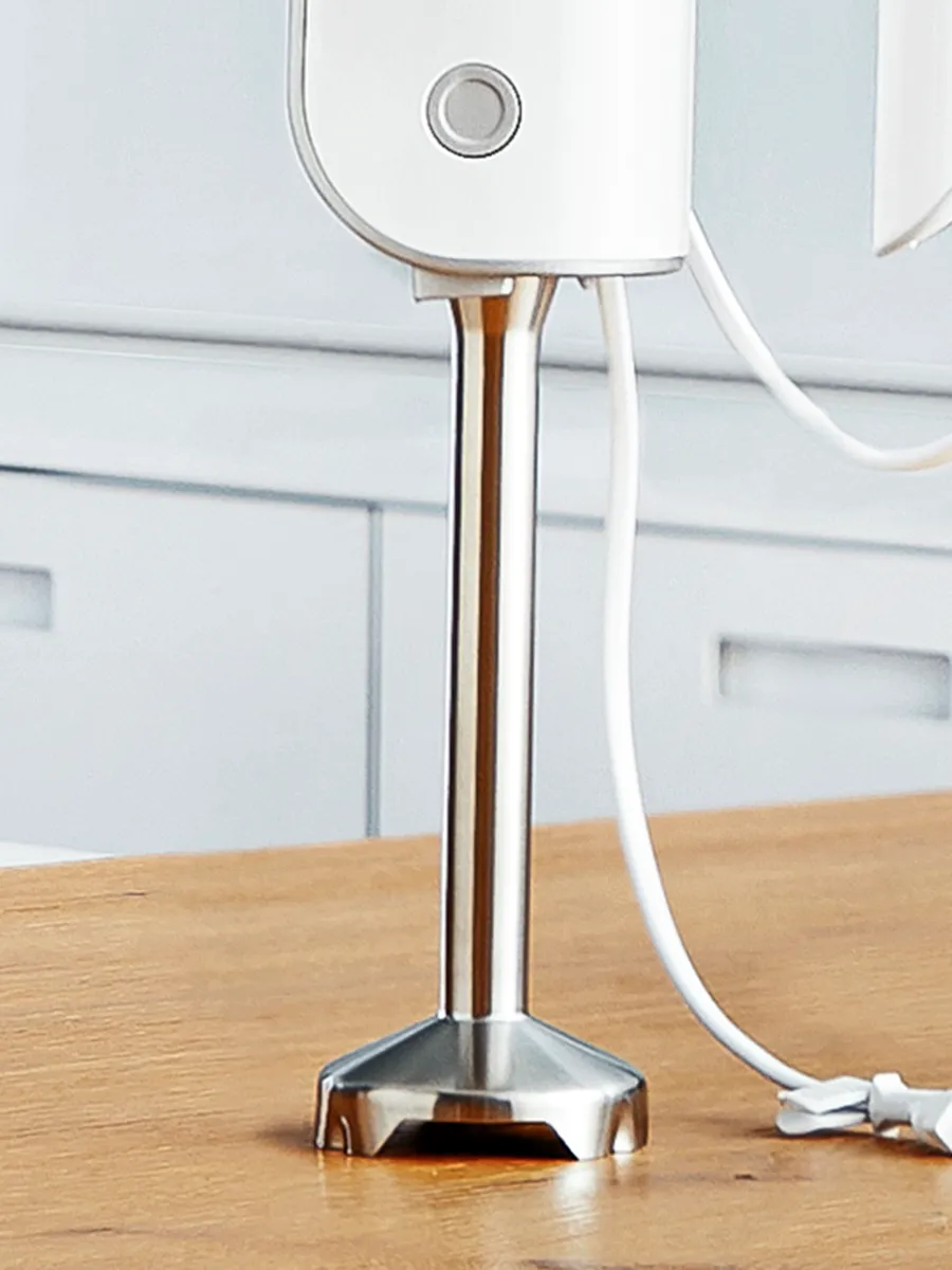 თანამედროვე სამზარეულოს გარემოში გამჭვირვალე თასის გვერდით შავი ხელის მიქსერი დევს, რომელშიც კარტოფილის პიურე, ნიგოზი და ხის კოვზია მოთავსებული.