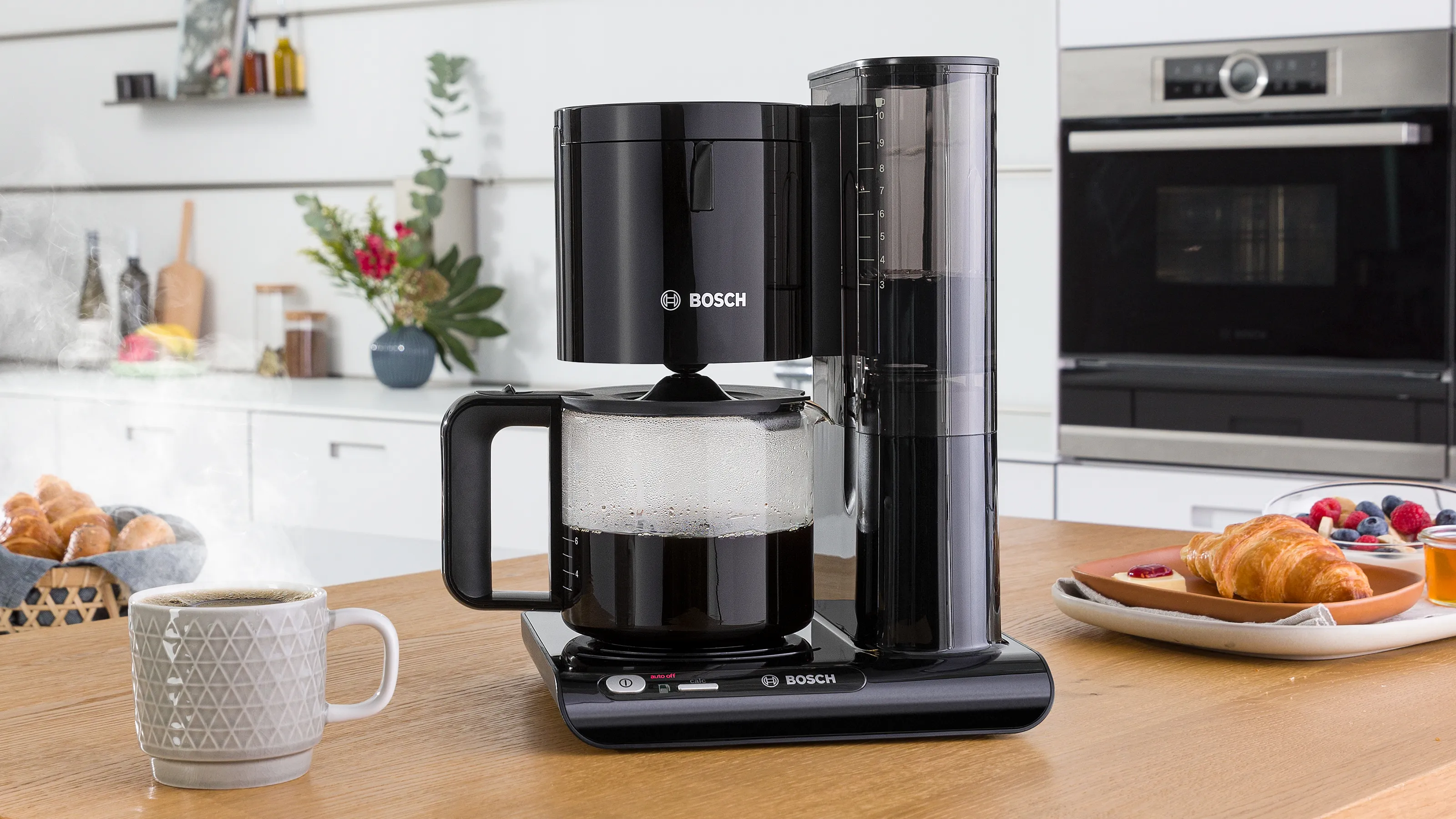 Filter coffee machine with carafe of coffee next to cups on kitchen counter.