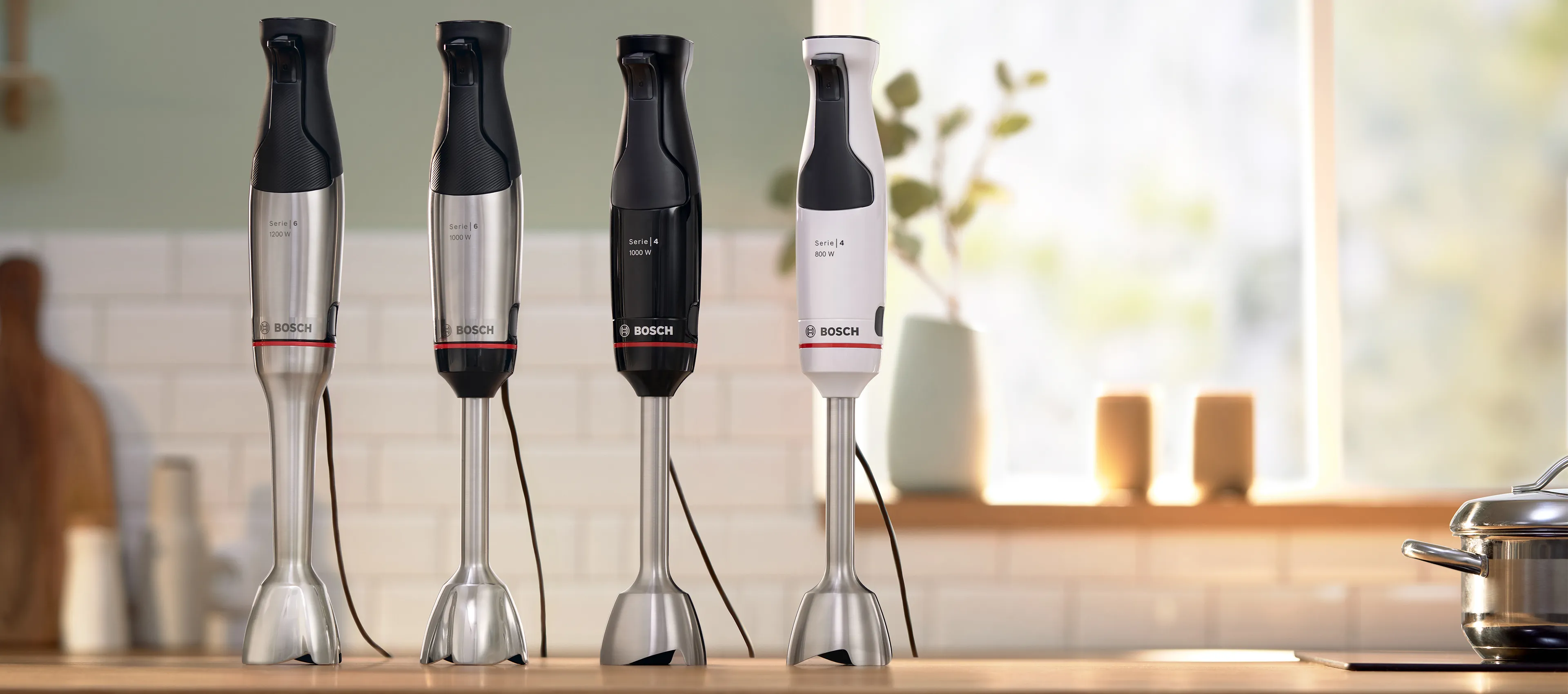 A selection of Bosch hand blenders standing on a wooden counter in a bright, airy kitchen.