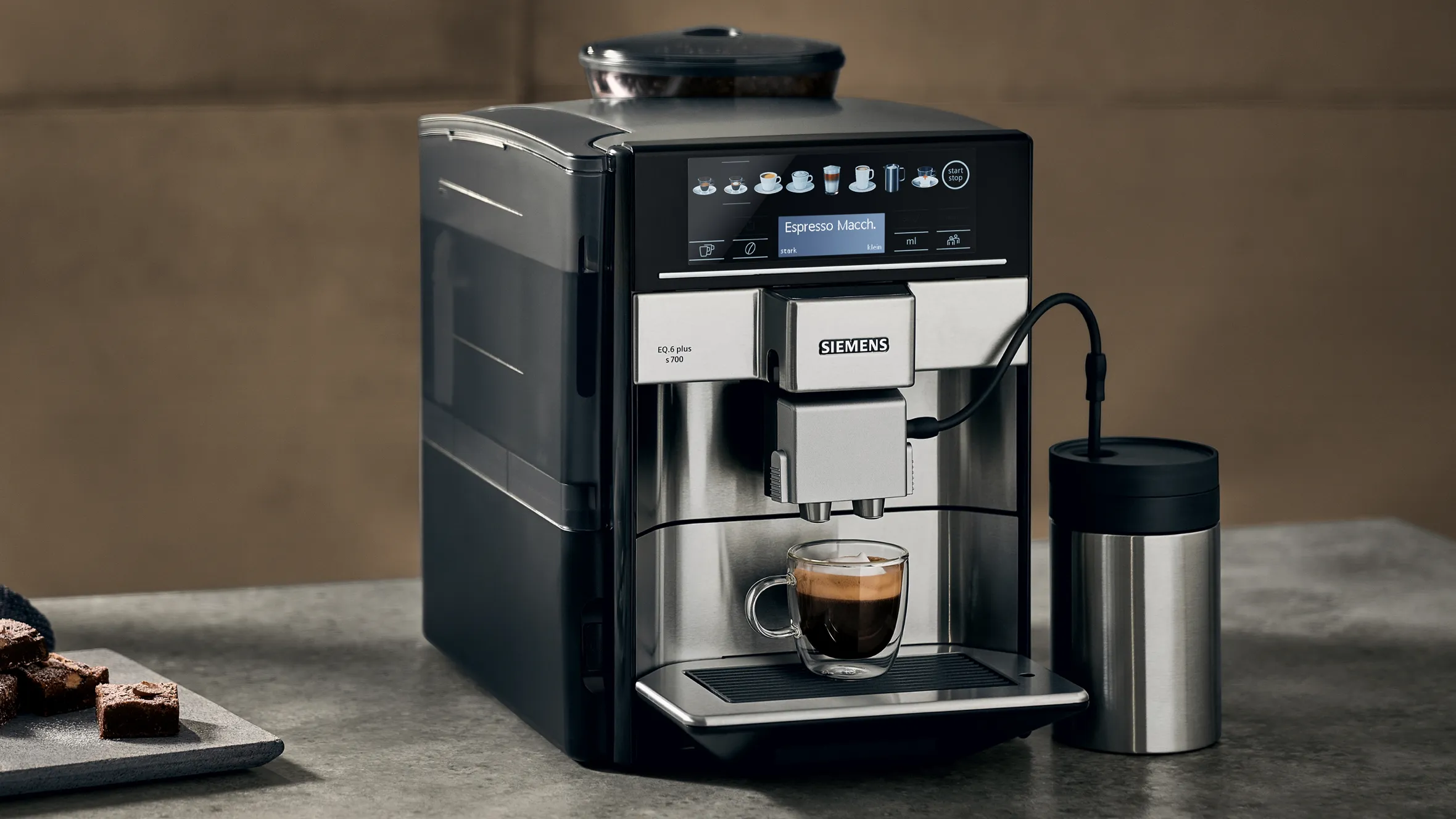 Sleek black coffee machine with digital display, dispensing espresso into a cup on a counter with baked goods.