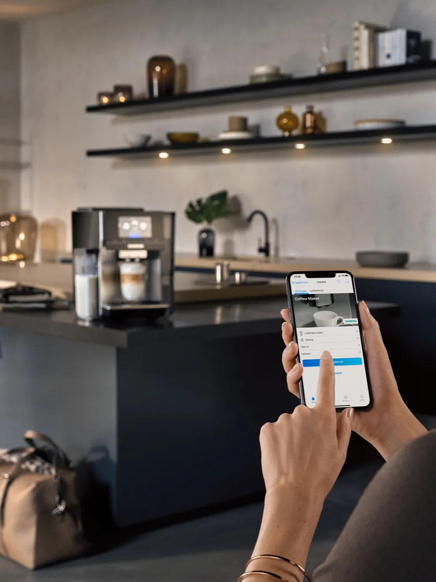 Kitchen interior with shelves, coffee machine, and person using smartphone app.