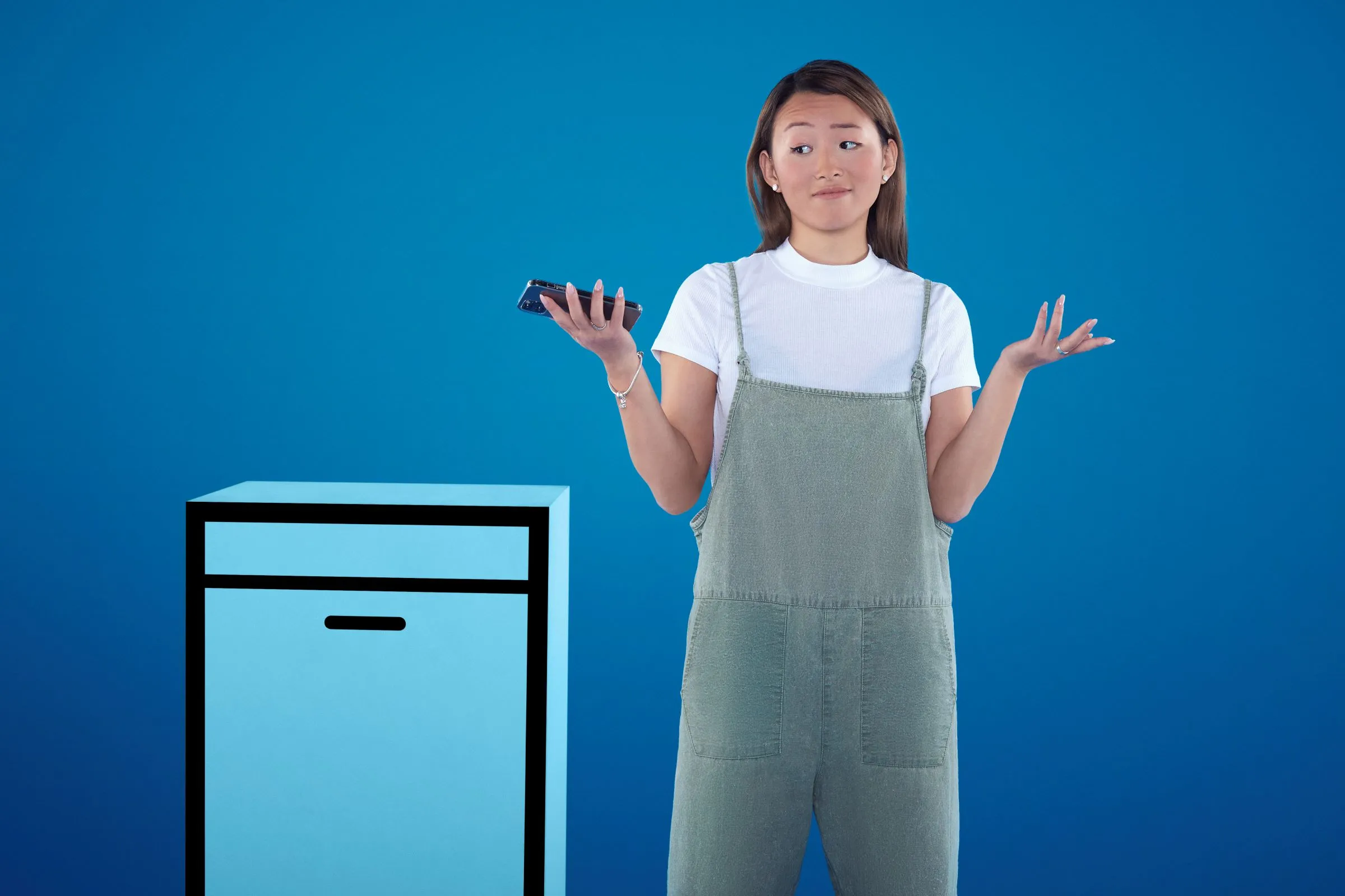 Young woman in casual outfit standing next to appliance, gesturing with hands, blue background.