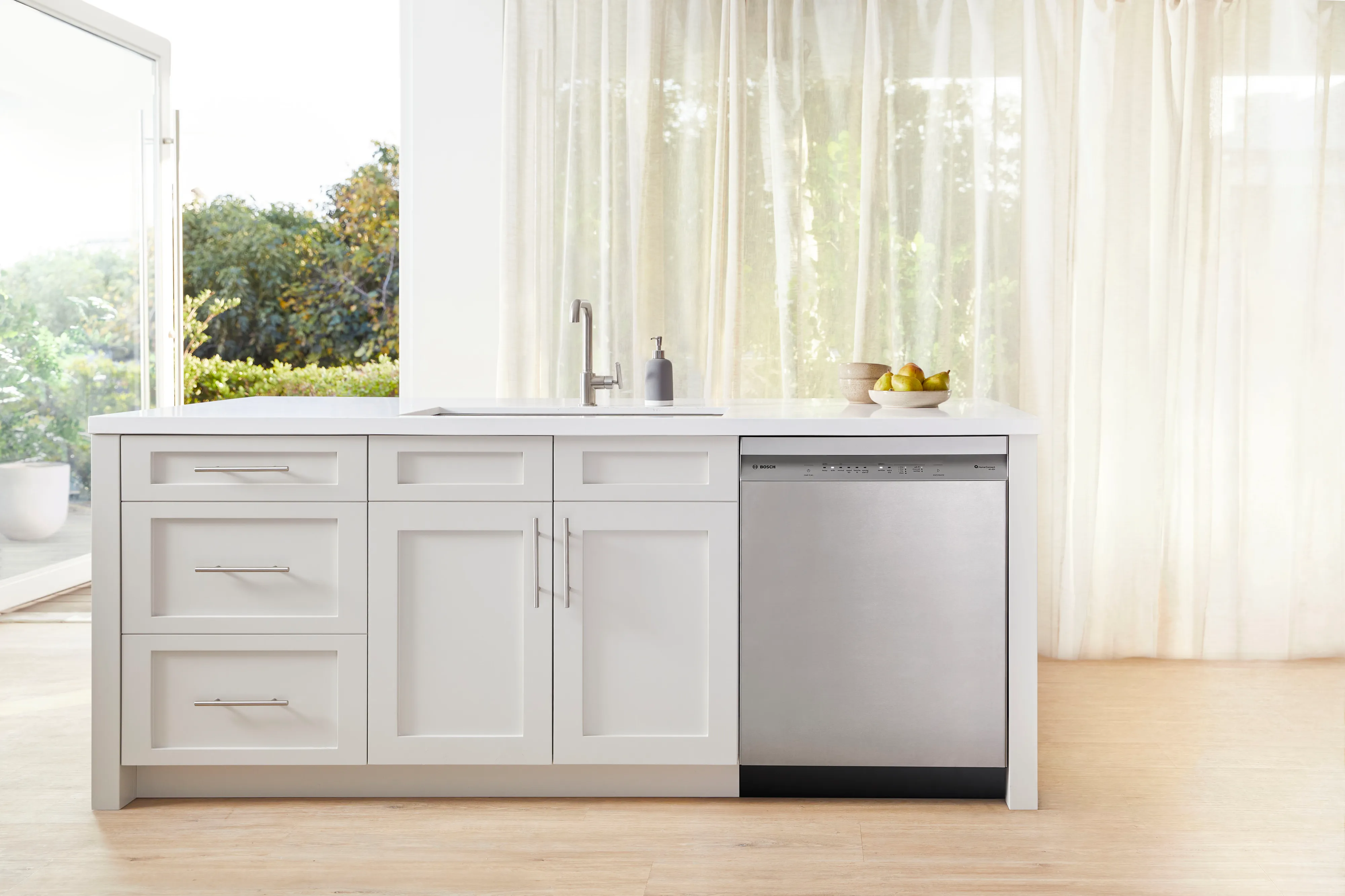Modern kitchen with a Bosch stainless steel dishwasher and white cabinets under a bright window.