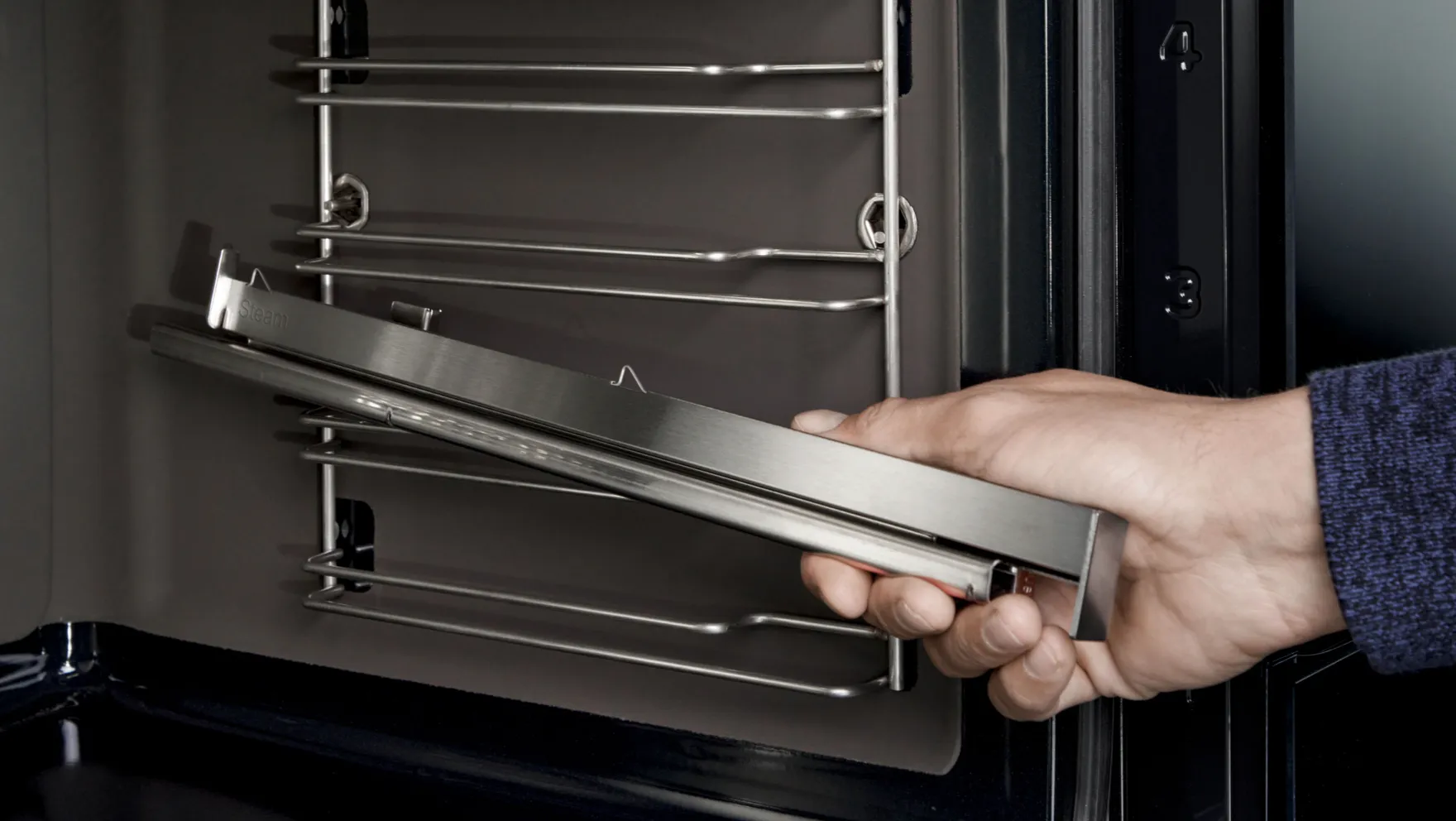 Hand opening oven door, revealing metal racks inside.