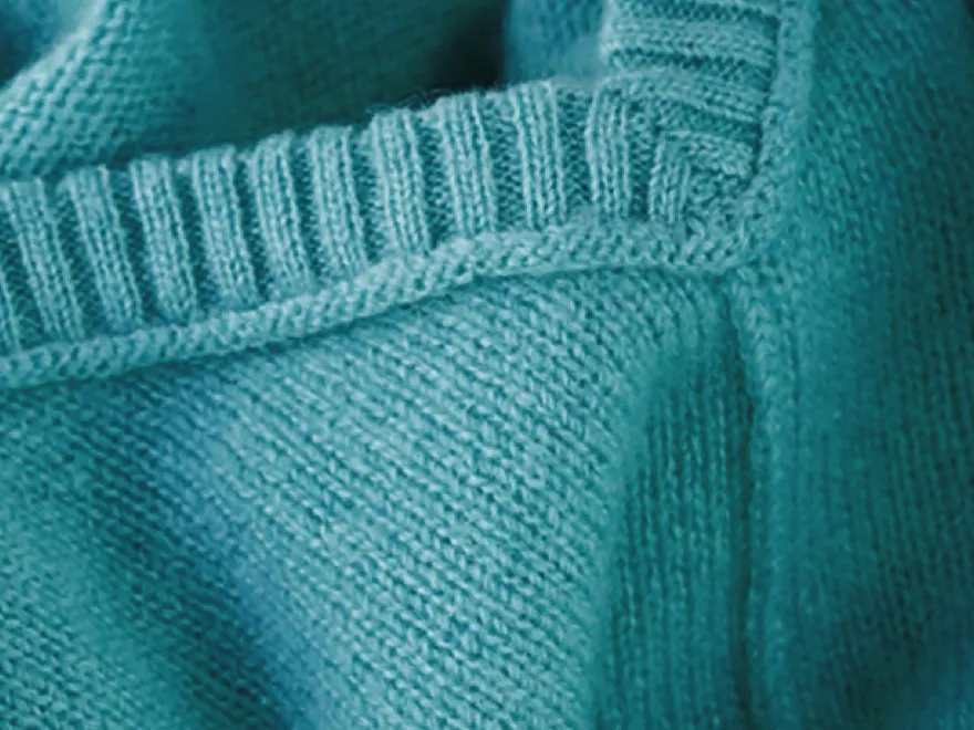 Closeup of a teal-colored knitted fabric with intricate patterns and textures.
