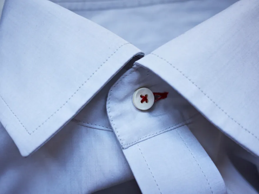 Close-up of a white dress shirt collar with a red button.