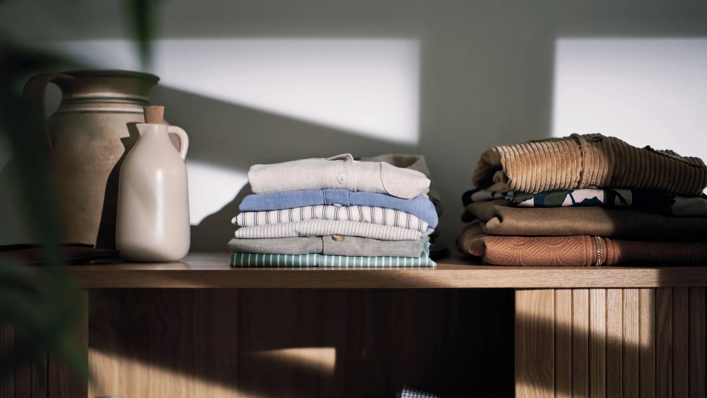 Stacked folded clothes, ceramic vase, and corrugated tubing on wooden shelves.