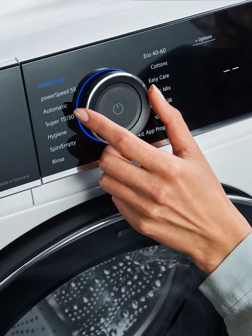 Hands operating washing machine controls, displaying various wash cycle options.
