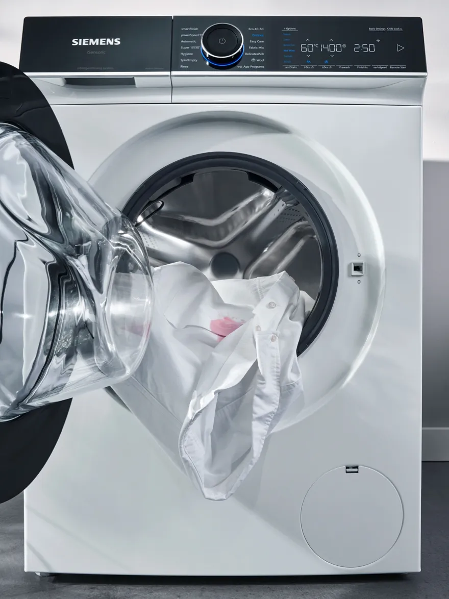 Washing machine with open door, revealing clothes inside, on a white background.