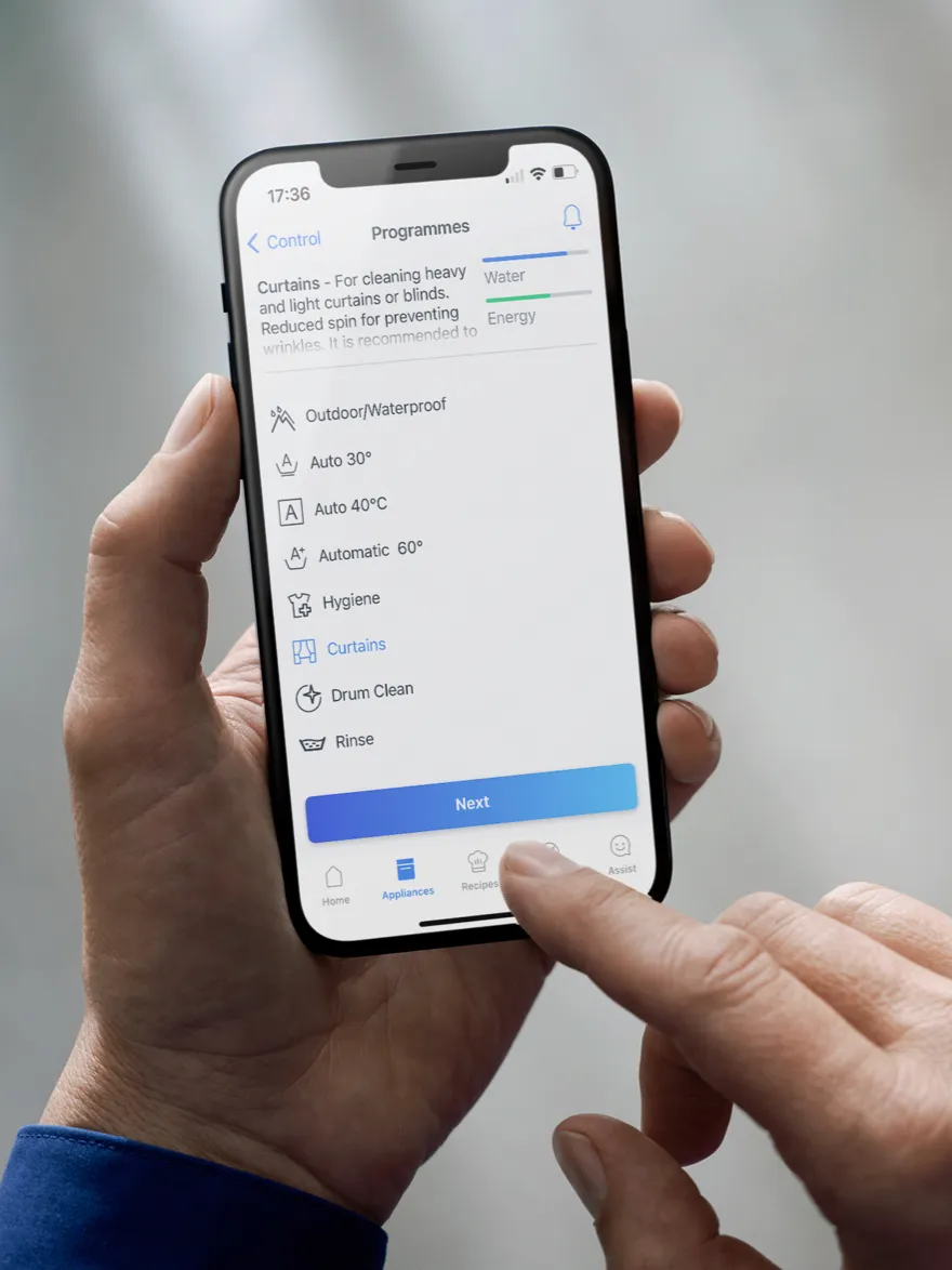 Smartphone displaying washing machine settings menu, hand holding device.