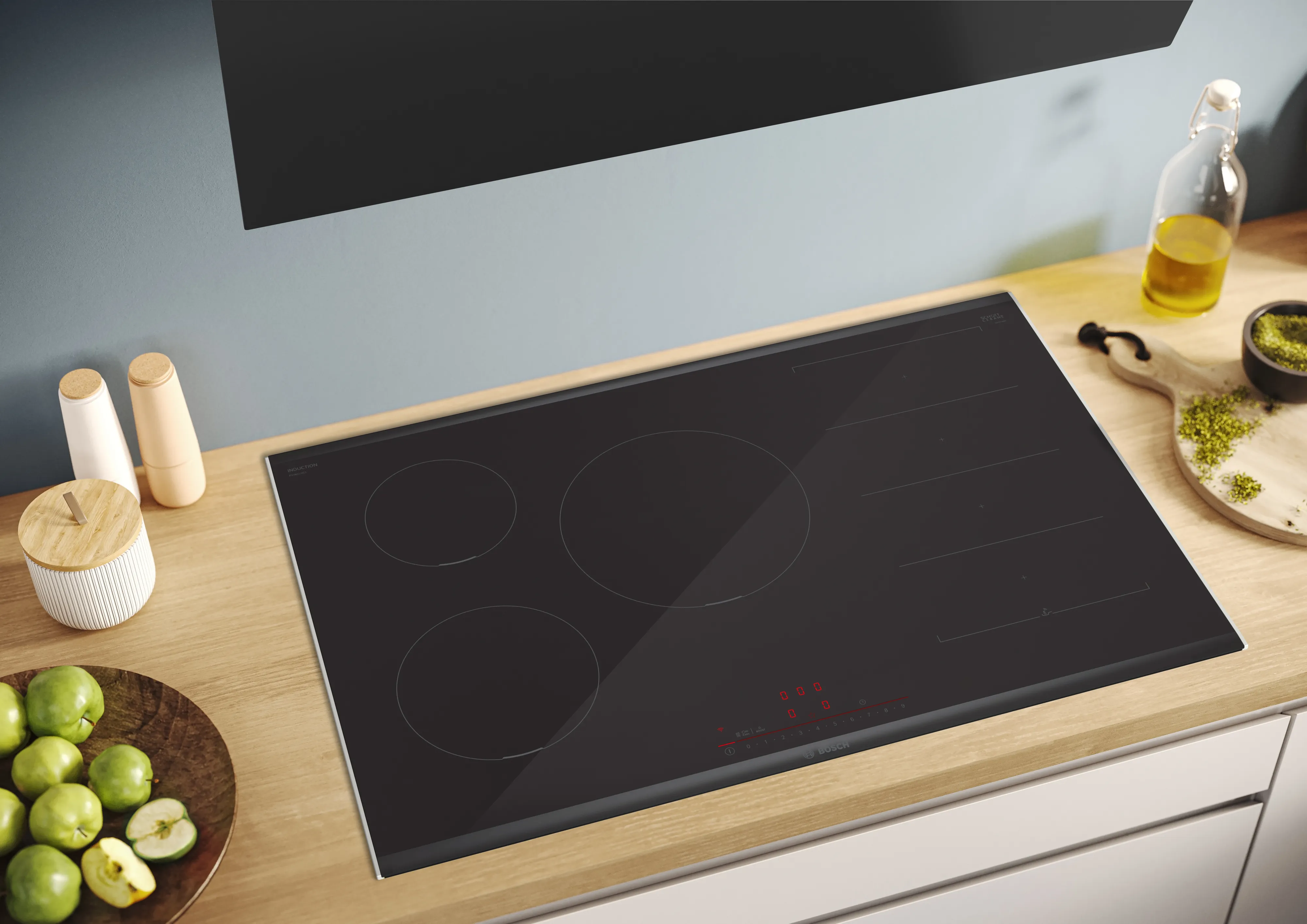 Elegante piano cottura a induzione nero su contatore cucina in legno con mele fresche e utensili da cucina.