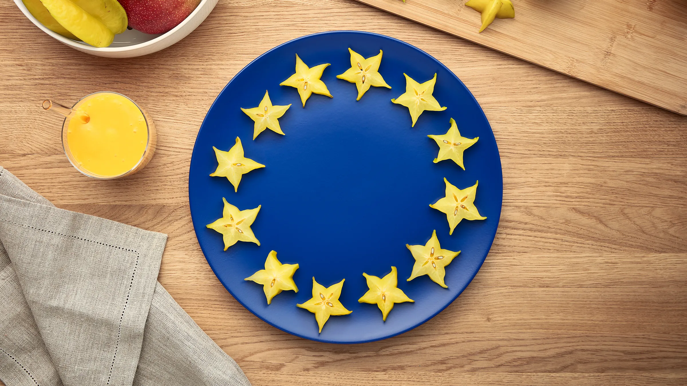 Blue plate with yellow star-shaped cookies arranged in a circle, surrounded by fresh fruit and a linen napkin on a wooden table.