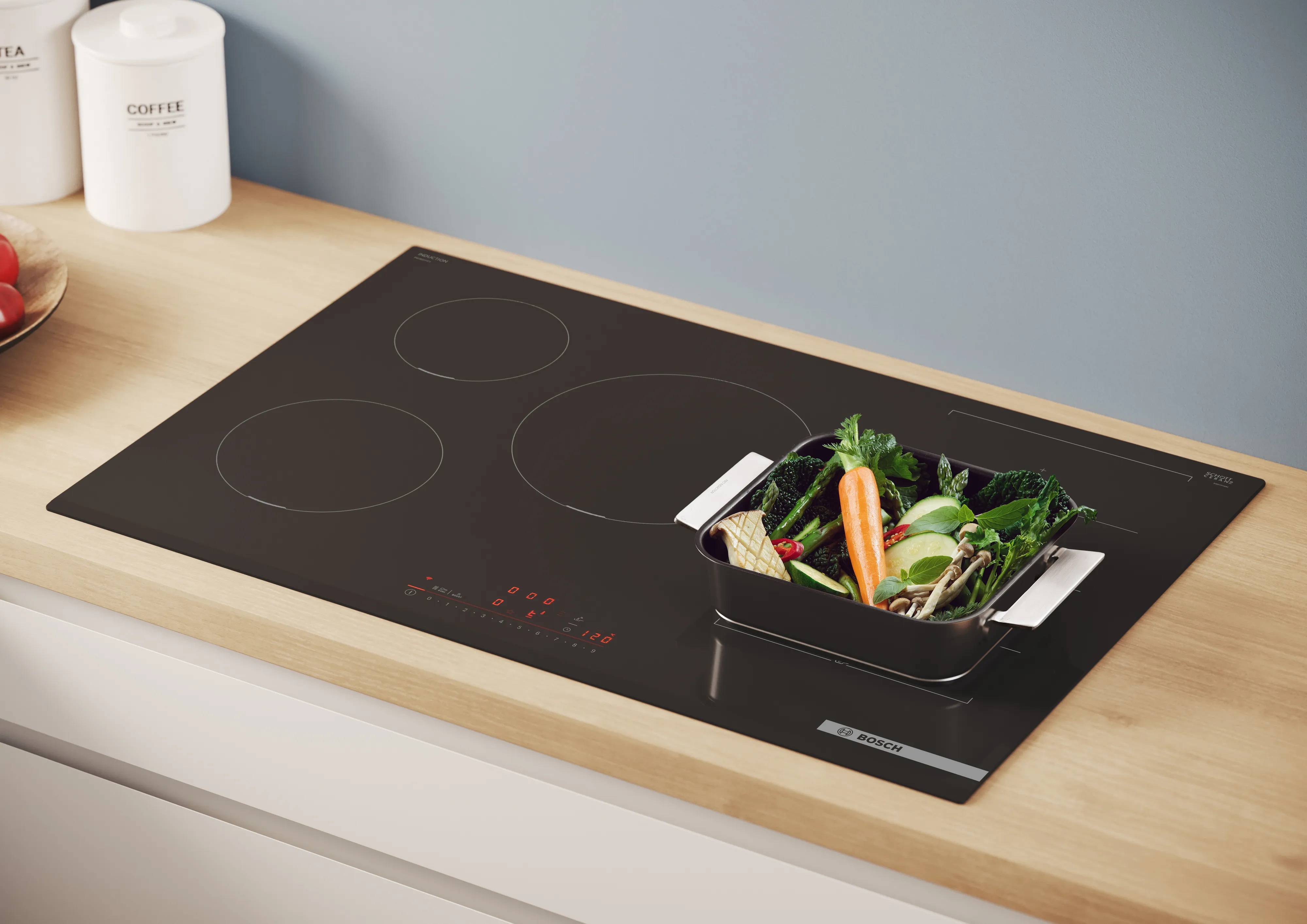 Piano cottura a induzione nero con pentola quadrata contenente verdure fresche