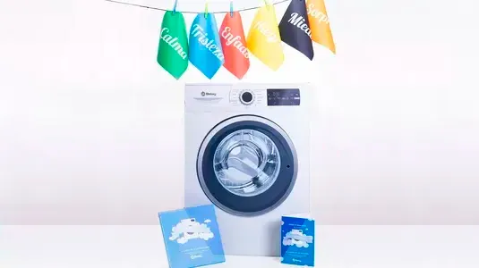 Lavadora con ropa de colores colgada, cajas de detergente y un fondo blanco. 
