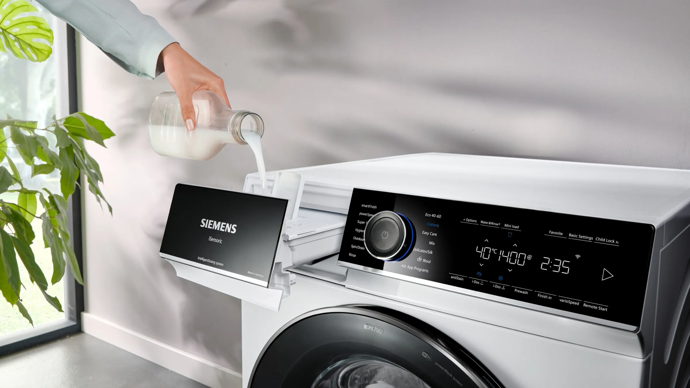 Washing machine with detergent dispenser, digital display, and houseplant in background.