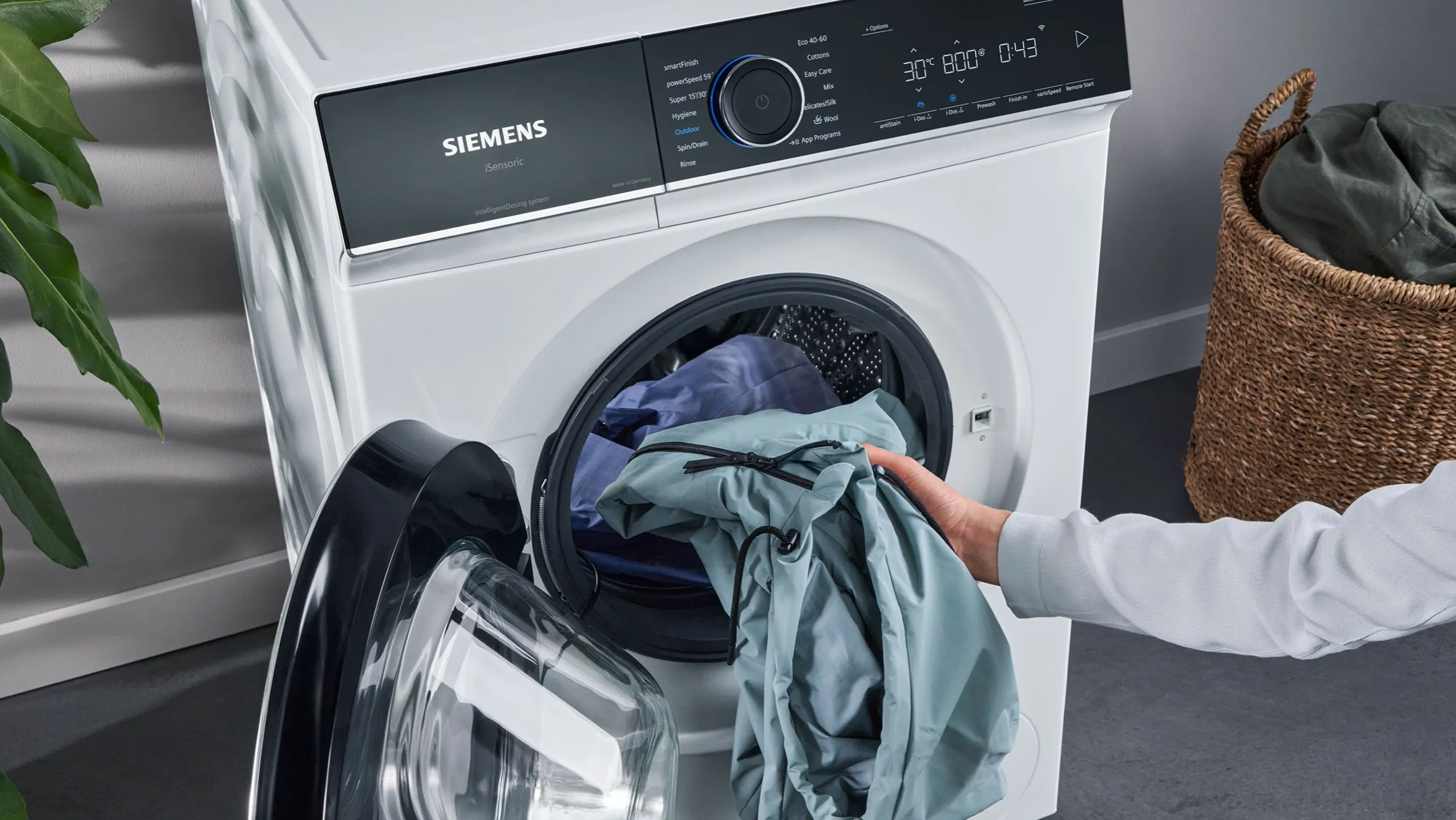 Washing machine with clothes being loaded, Siemens brand, modern appliance, laundry, household chore.