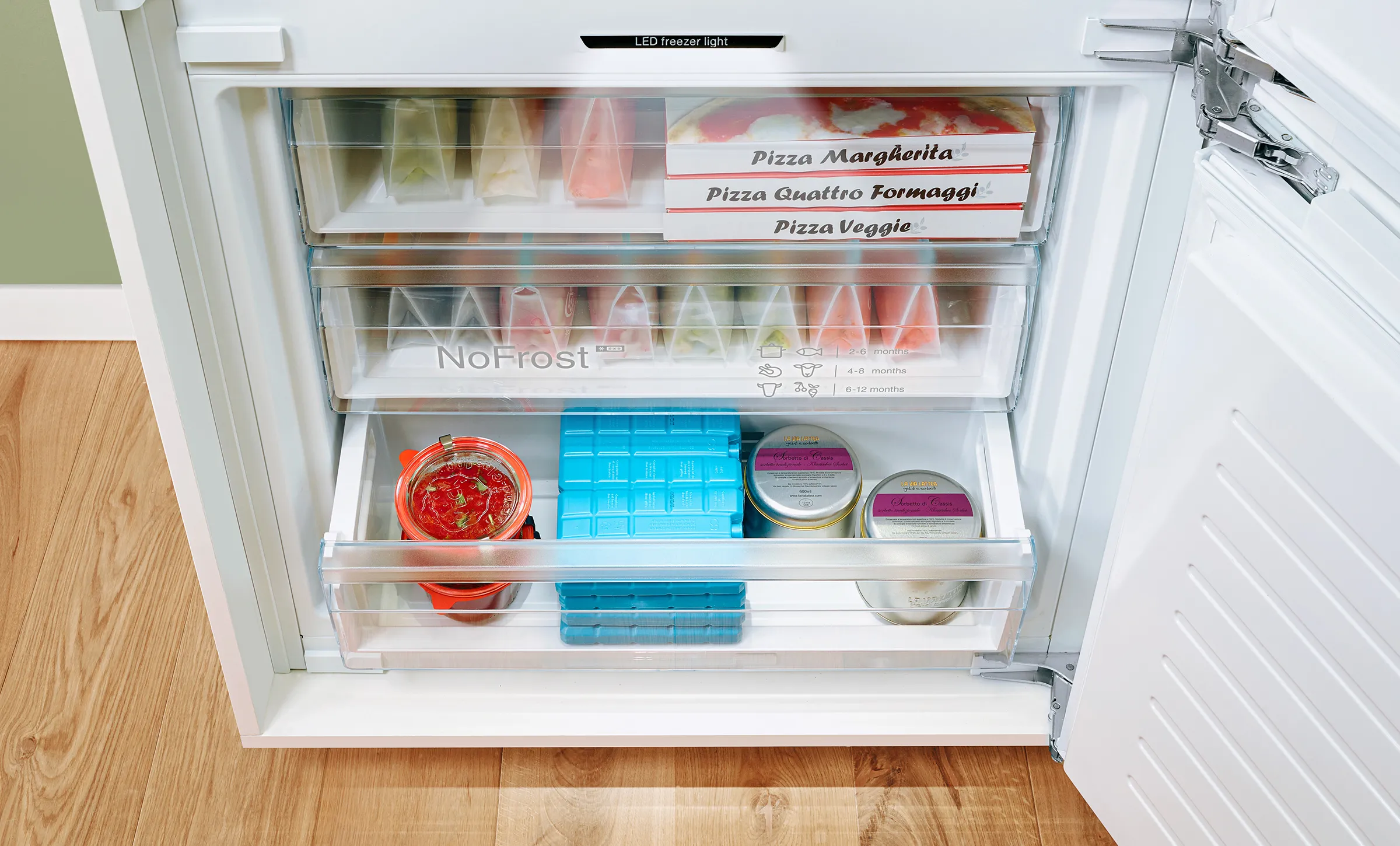 Aprire il frigorifero con vari prodotti alimentari, tra cui scatole di pizza, contenitori e altre forniture di cucina.