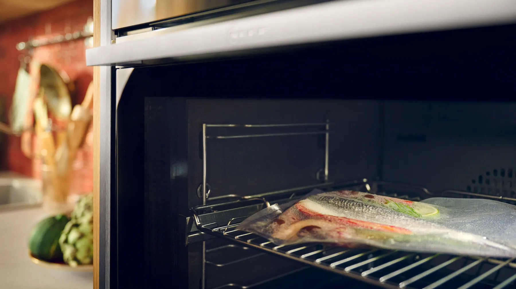 Primo piano di un pesce avvolto nel sottovuoto su una griglia all'interno di un elegante forno, con uno sfondo caldo della cucina visibile.