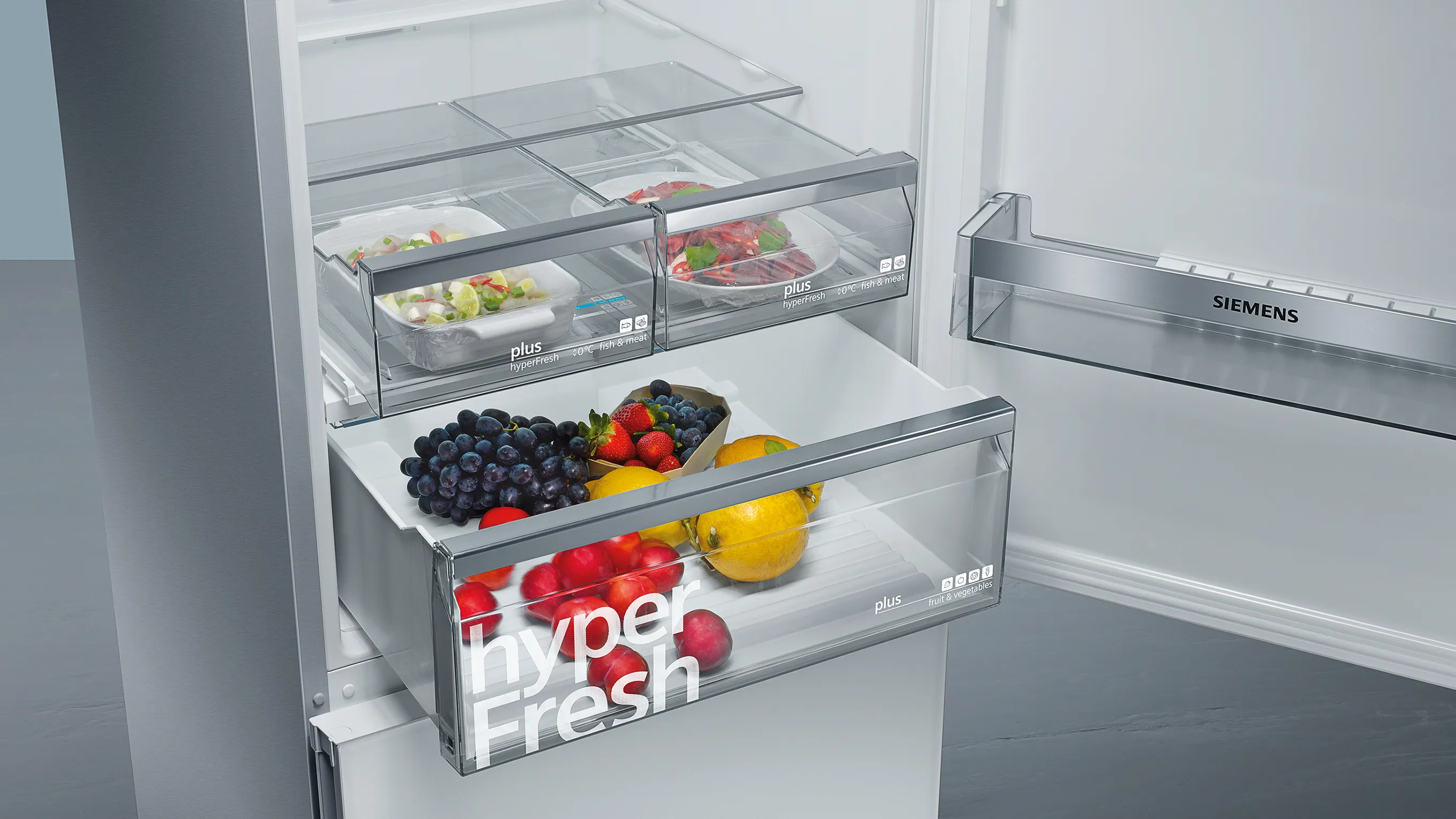 Un réfrigérateur Siemens ouvert dans lequel on aperçoit un tiroir hyperFresh rempli de fruits et légumes frais.