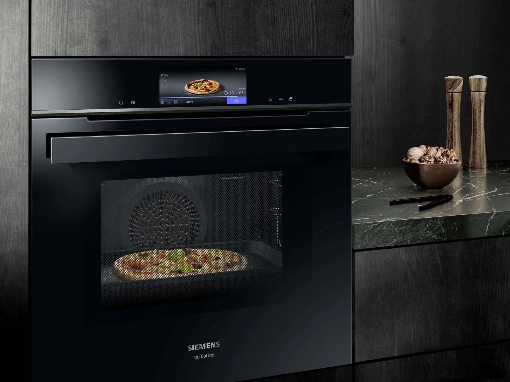 Black built-in oven with pizza inside, marble countertop, kitchen appliances.