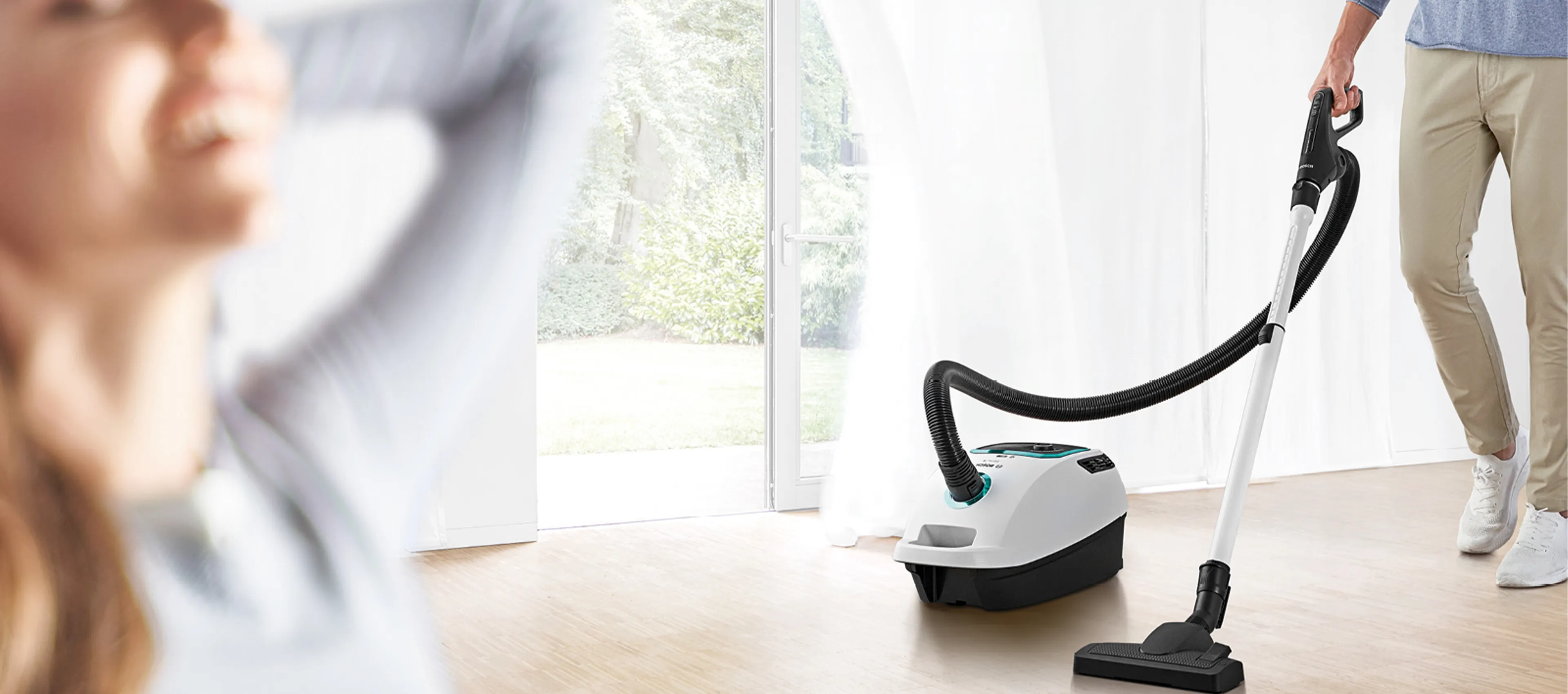 Two Bosch vacuum cleaners in navy blue and black beside a light-colored rug in a bright, modern living room.
