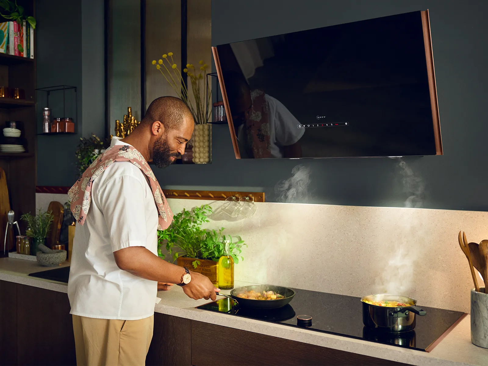 Man in white chef's uniform cooking in kitchen with TV screen in background.