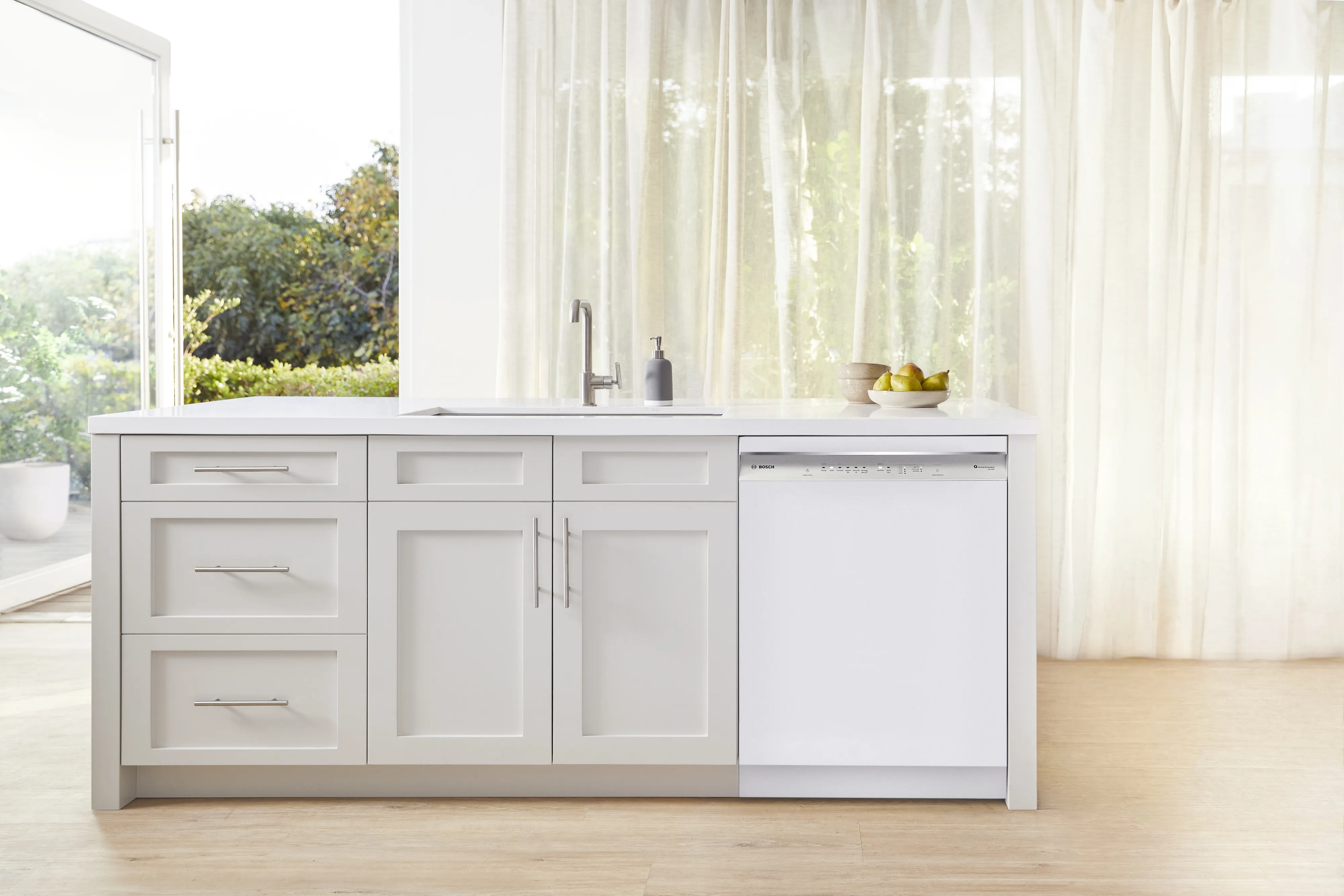 Modern kitchen with white cabinets, island, and Bosch dishwasher by a large window.