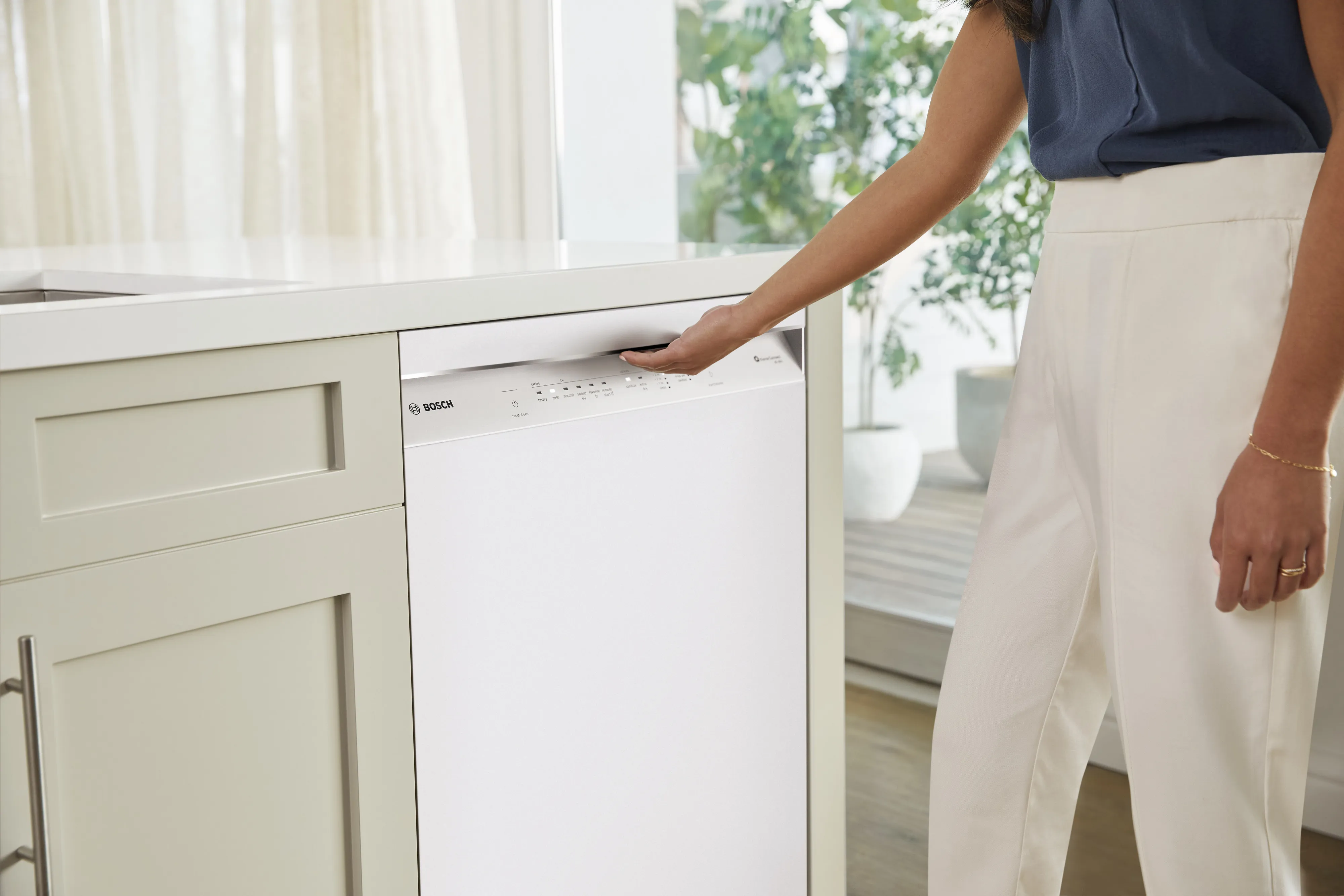 woman operating a Bosch dishwasher integrated into a modern kitchen cabinet.