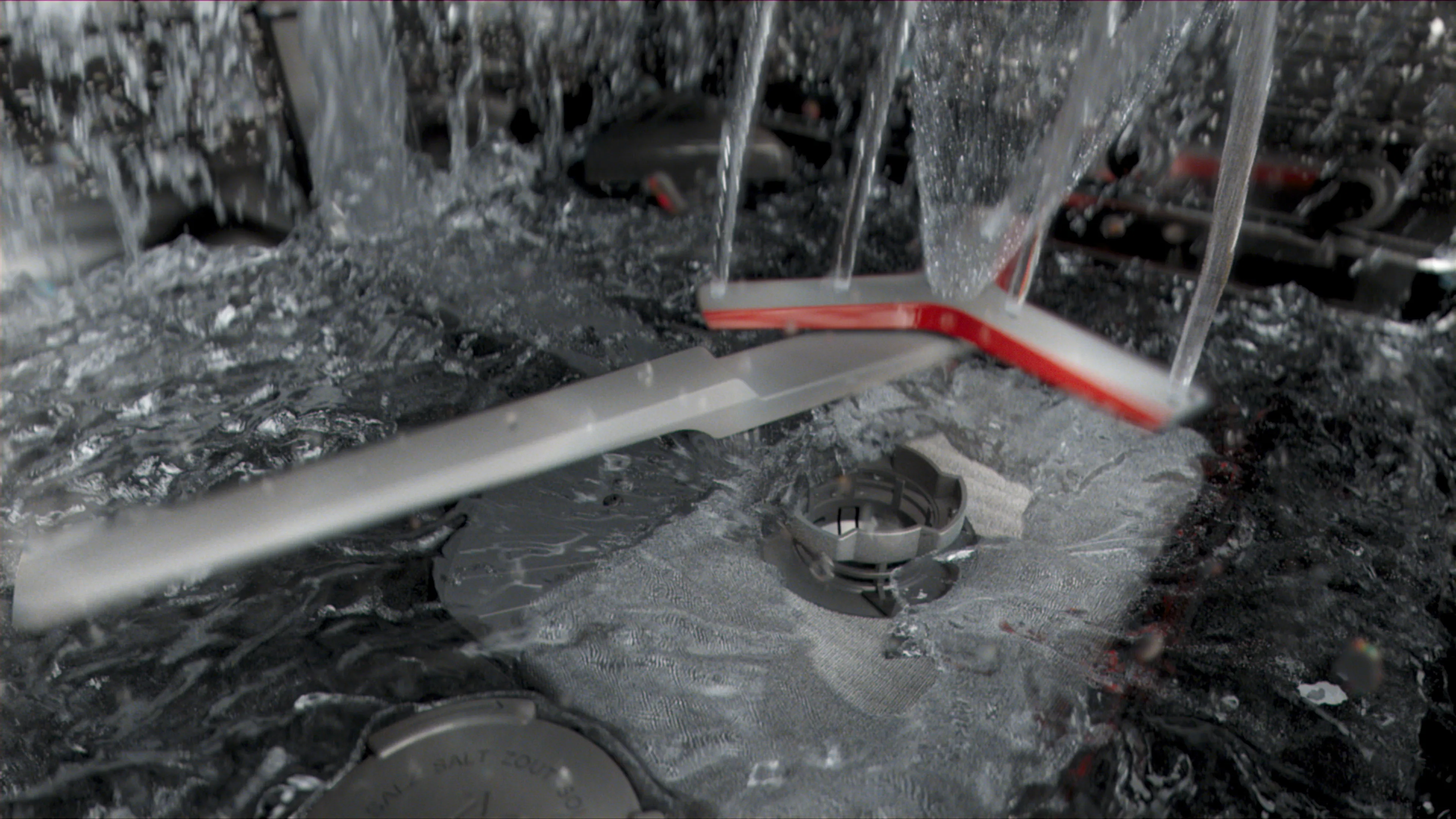 Sprinkler system spraying water on a dark, rocky surface with metal components visible.