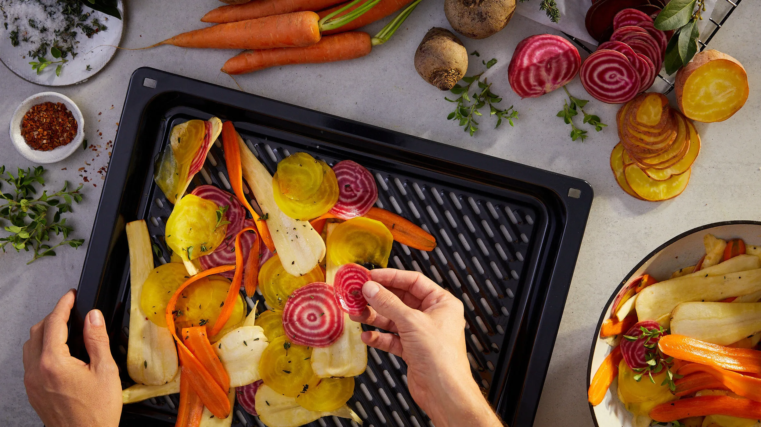 Roasted vegetables on baking tray, hands arranging food, colorful assortment of carrots, potatoes, beets.