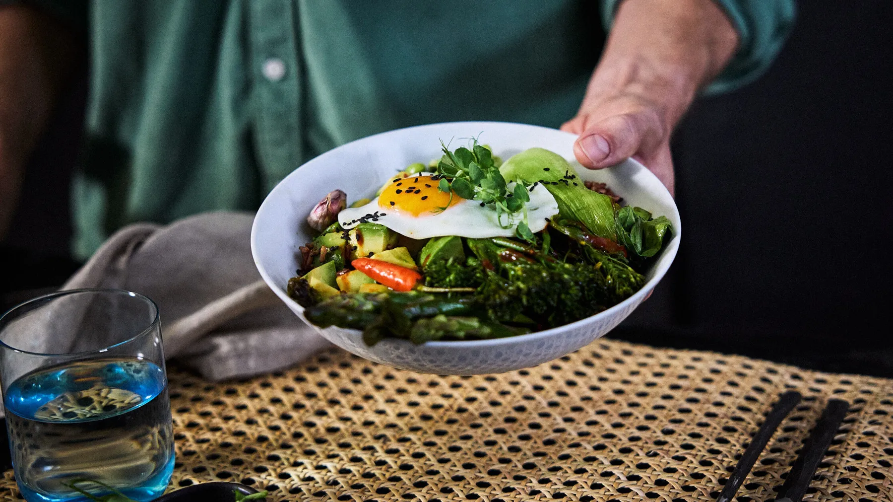 Healthy vegetable salad with fried egg, served on a table with a glass of water.