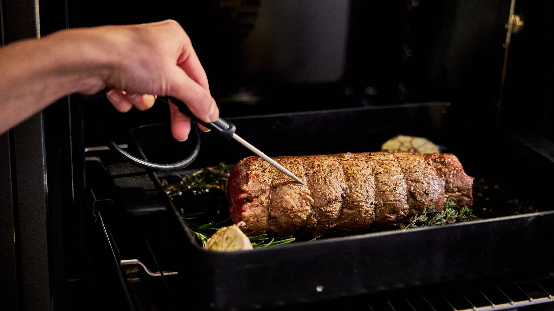 Geröstetes Fleischgericht wird im Ofen zubereitet, mit Hand halten Utensilien zum Basteln oder überprüfen Sie das Essen.