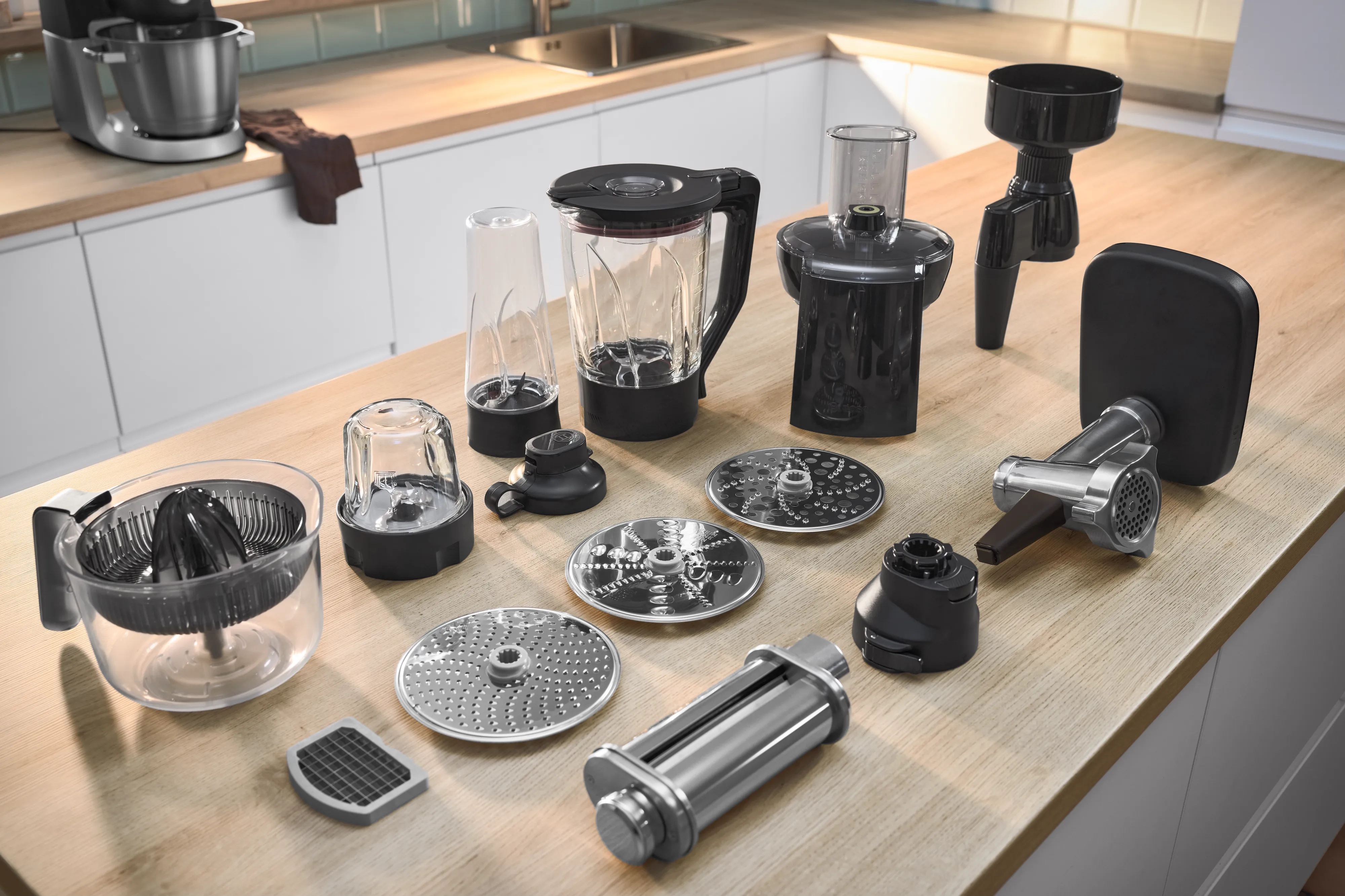 Una moderna scena di cucina con un mixer Bosch nero e un robot da cucina su un piano di lavoro in legno, con un'insalata colorata e verdure a fette nelle vicinanze.