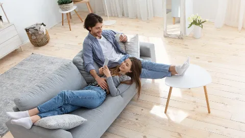 Couple relaxing on couch, smiling, casual clothing, modern living room.