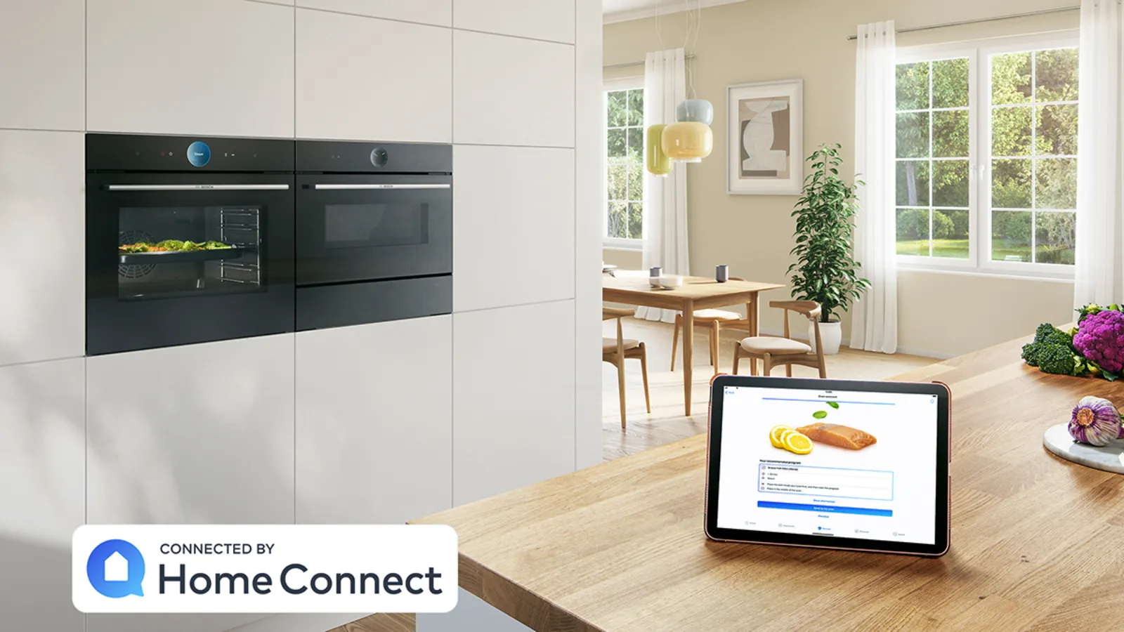 Modern kitchen with smart home device, dining area, and large windows overlooking outdoor scenery.