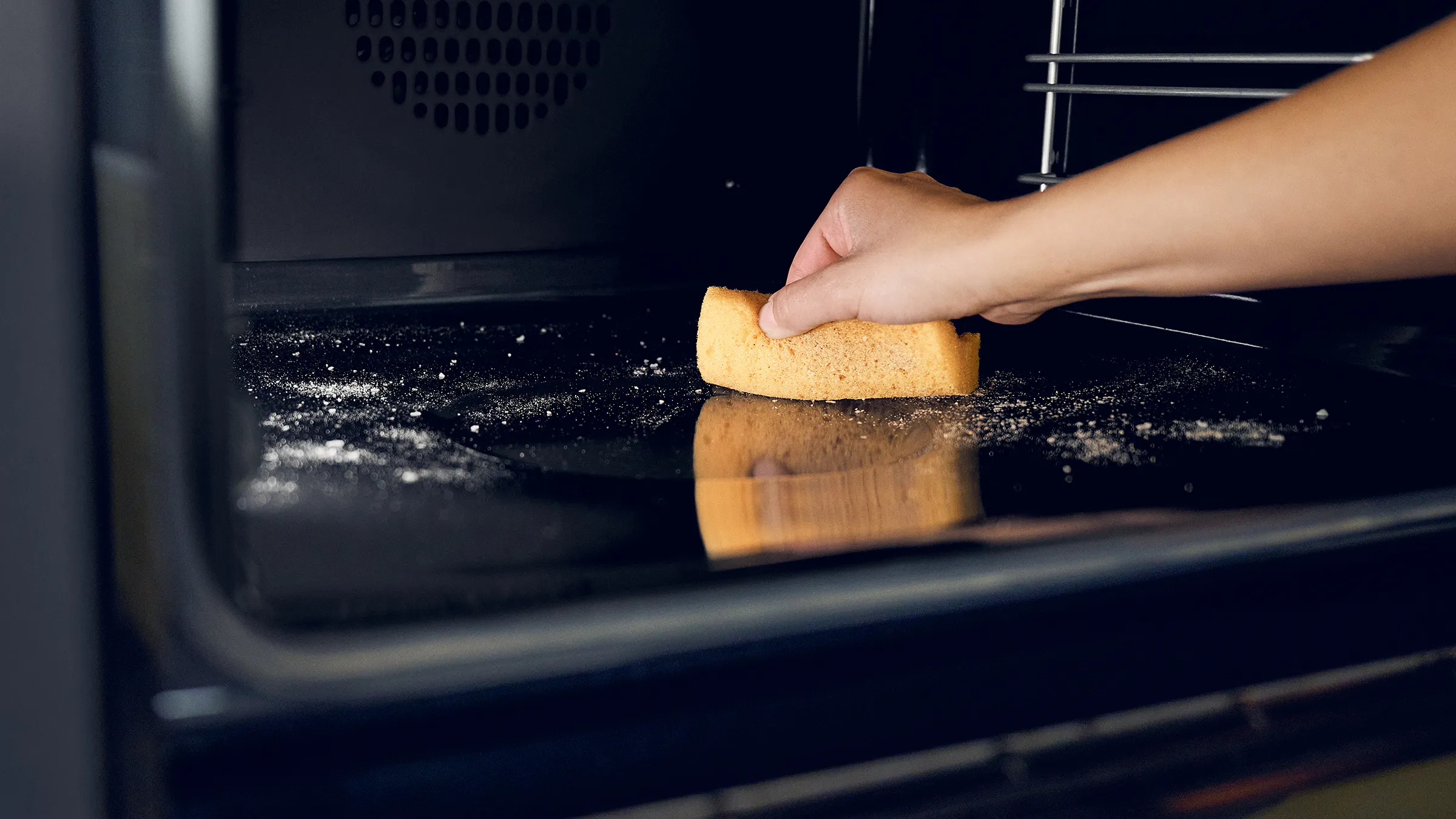 Hands placing a slice of bread in a dark oven, with flour visible on the surface.