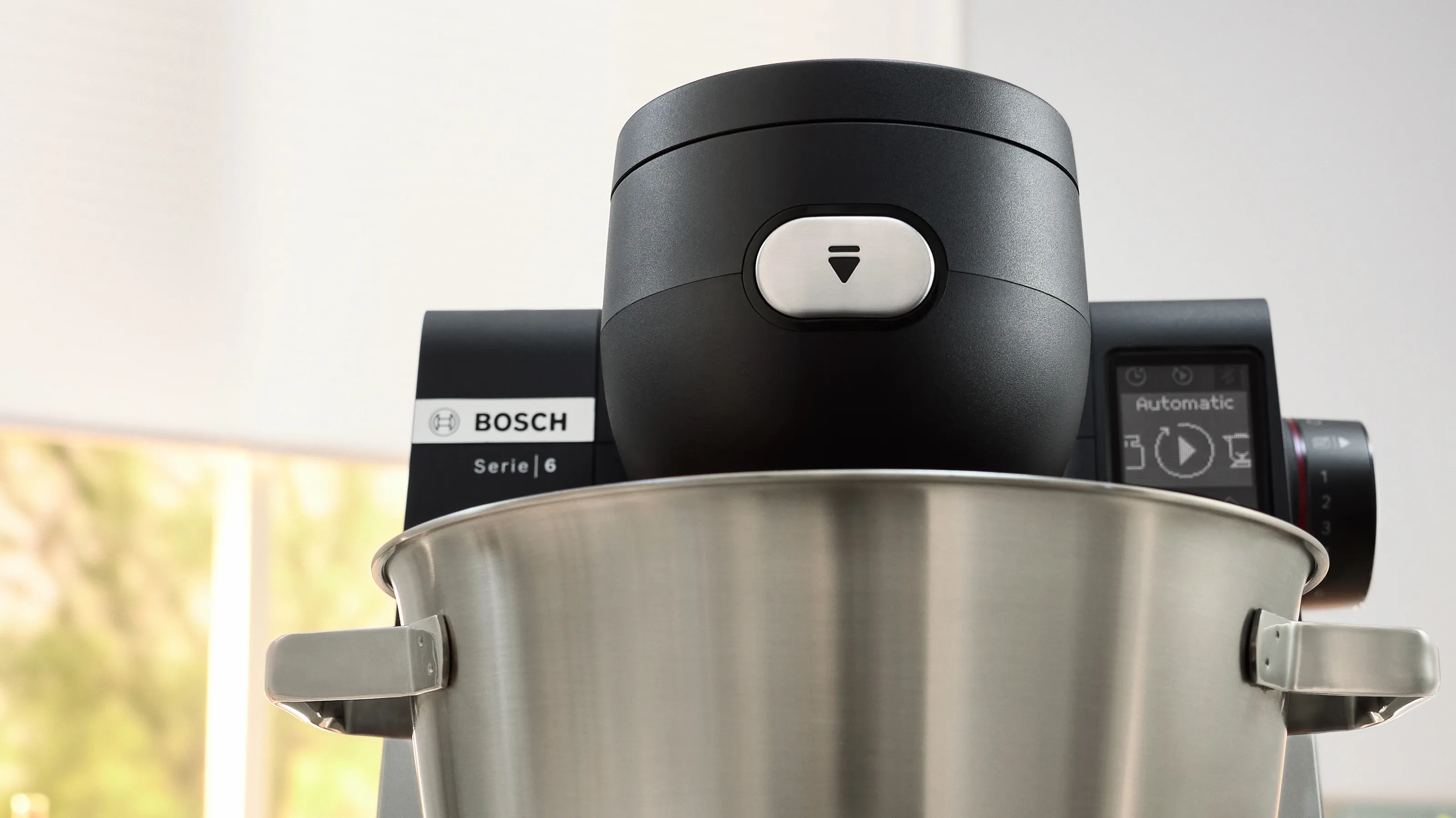 Gros plan d'un robot pâtissier Bosch Serie 6 noir avec un bol en acier inoxydable, affichant son panneau de commande et sa balance intégrée