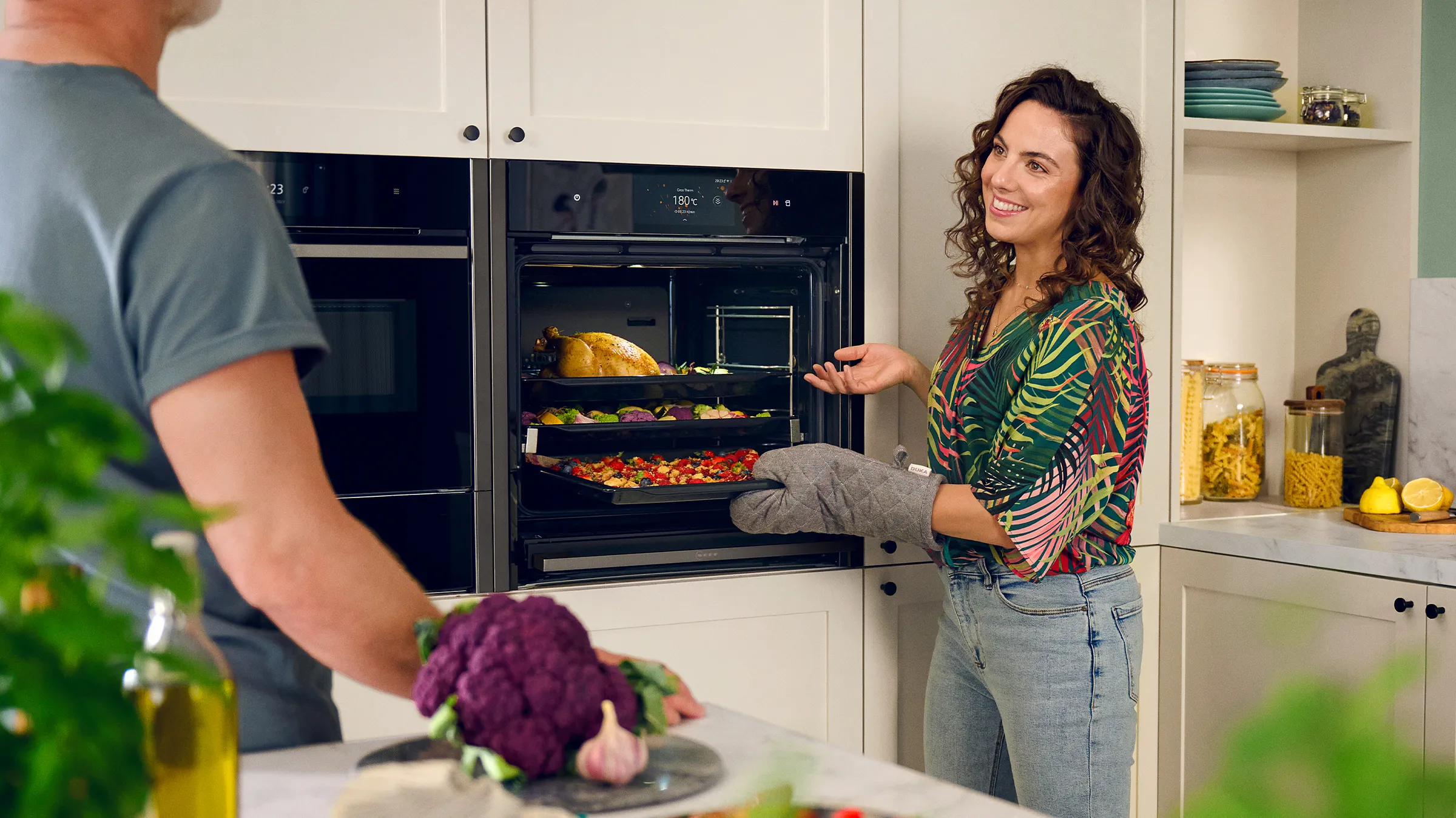 A woman and a man collaborate in a kitchen, standing near an oven, engaged in cooking activities together.