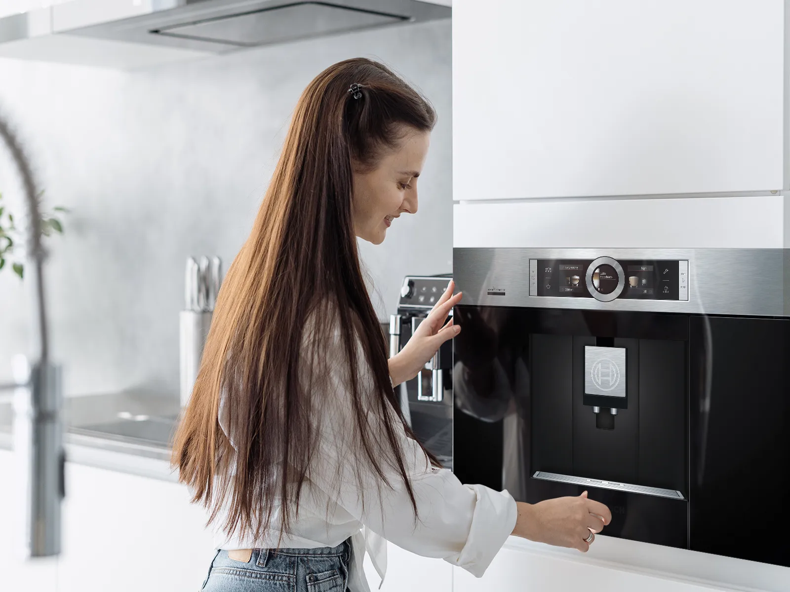 Woman with long brown hair operating coffee machine in modern kitchen.